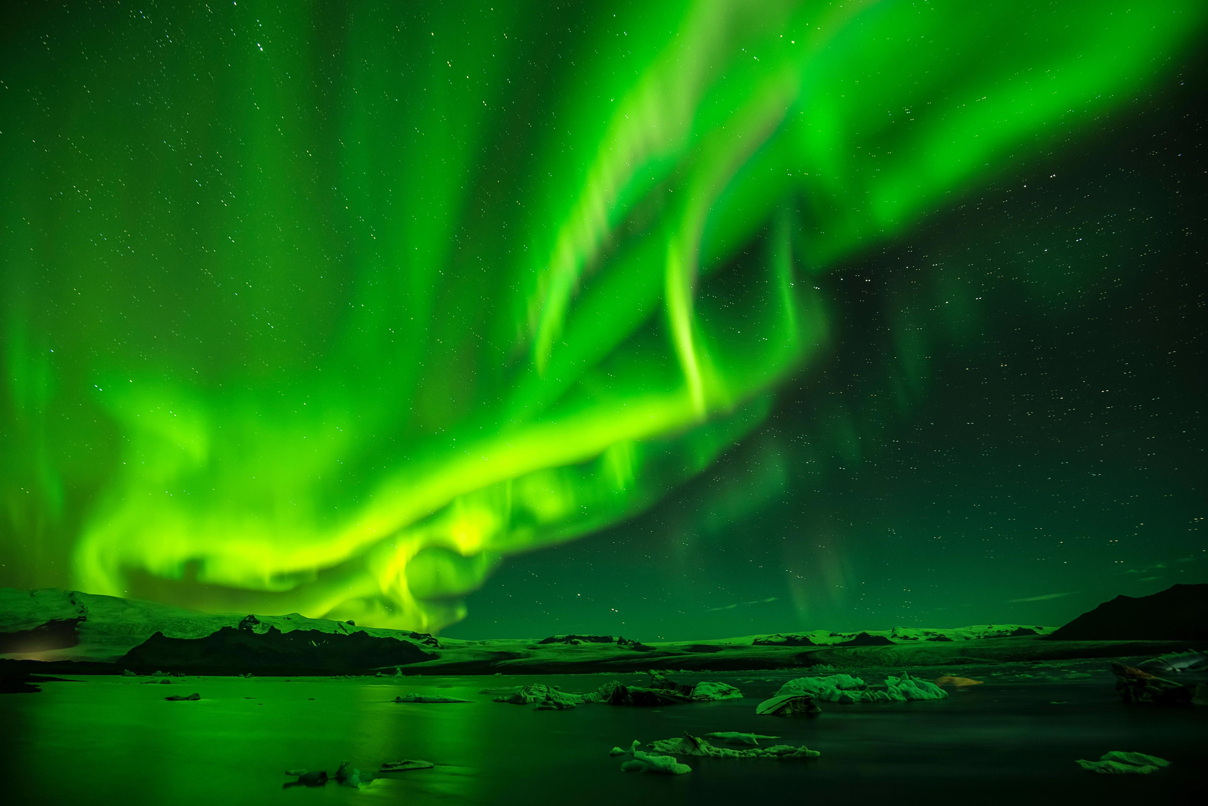 Vibrant green aurora borealis over a dark lake with floating ice.