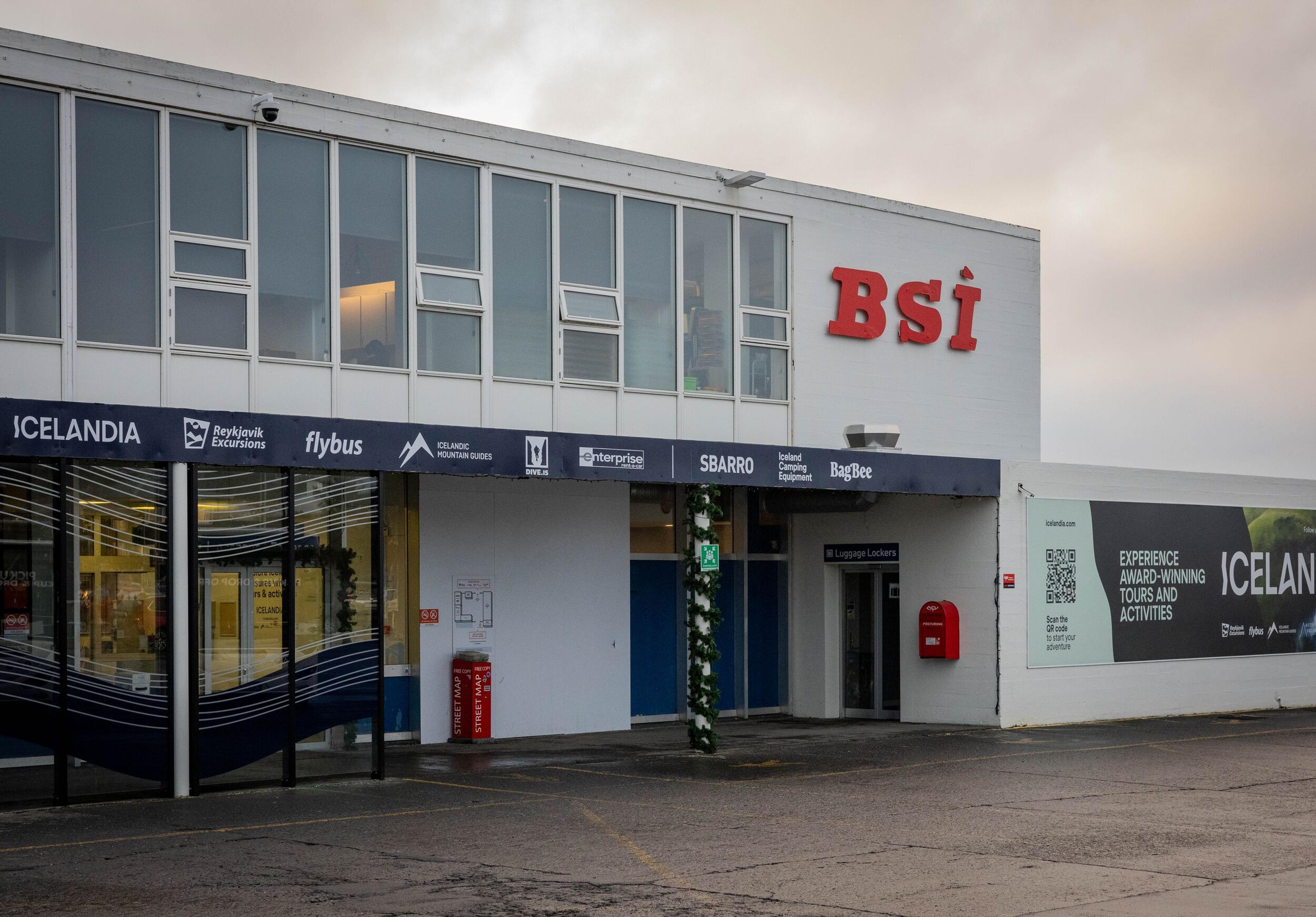 Exterior view of the BSI terminal building, displaying a red "bsi" sign and logos for companies like Flybus, Icelandia, and Reykjavik Excursions.