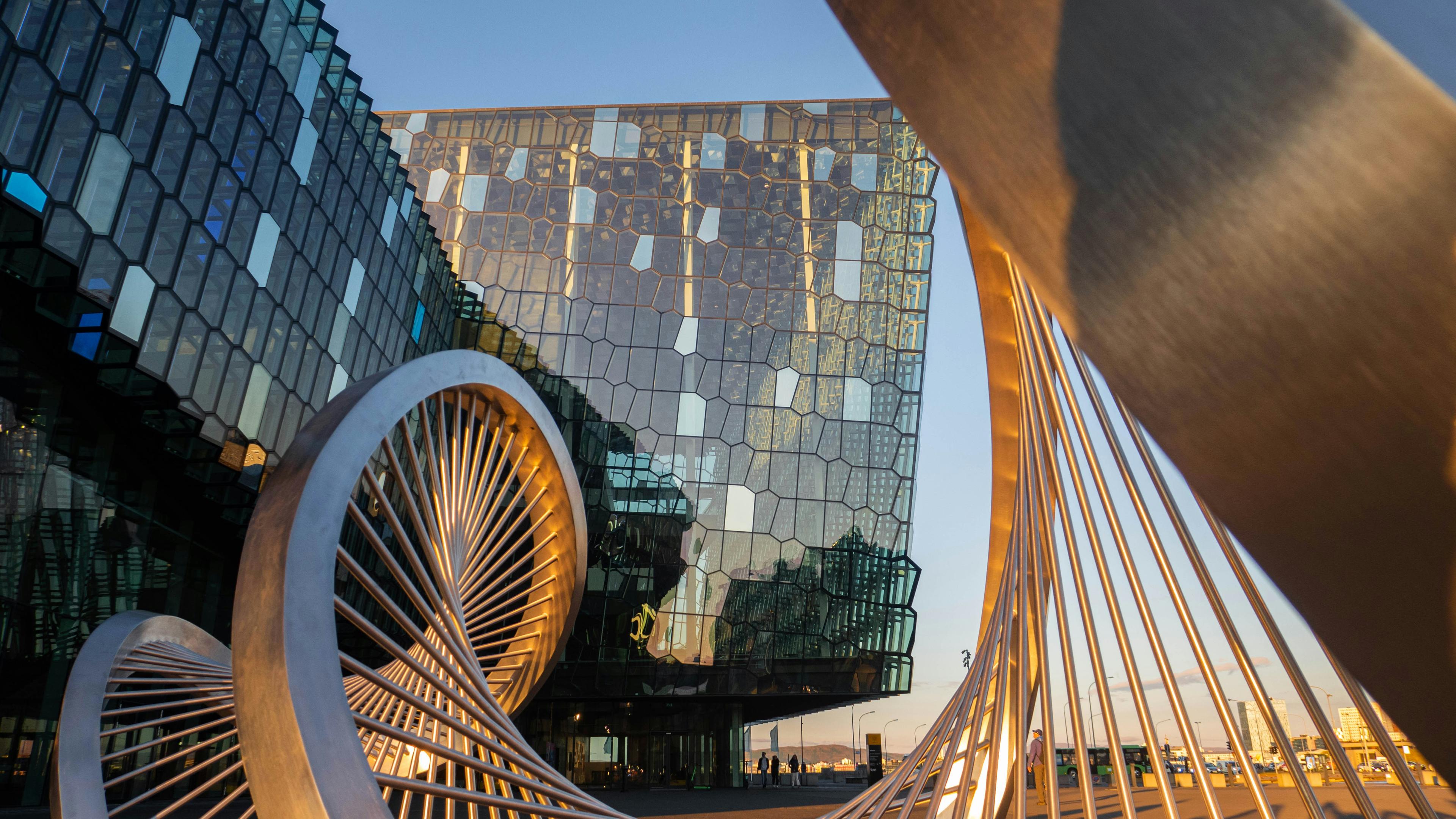 Modern architectural building with a geometric glass facade, featuring unique metal sculptures in the foreground under clear skies.