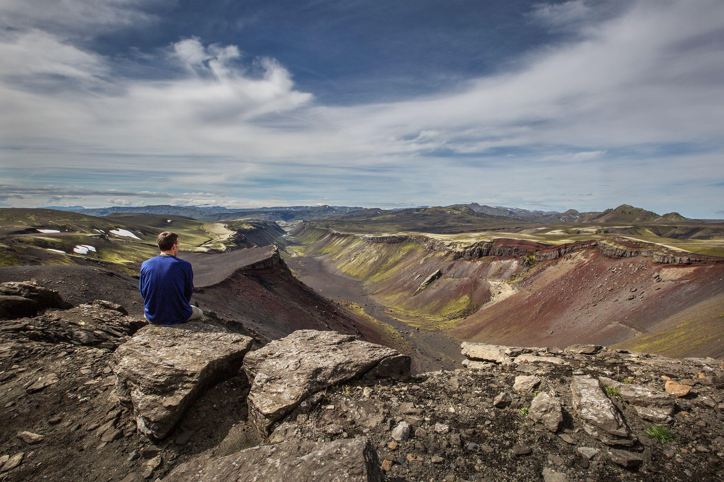Man sitting atop a mountain, taking in the expansive view and serene landscape.