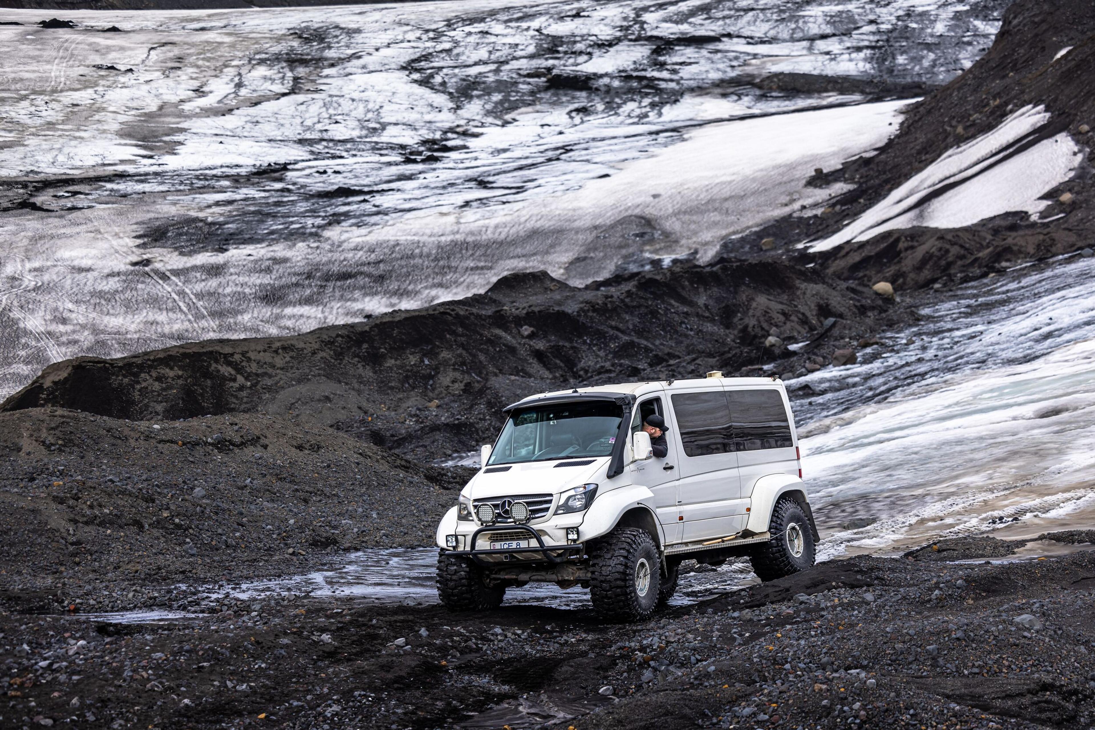 hite 4x4 vehicle driving on a glacier in Iceland, navigating through a mix of icy slopes and rocky terrain.