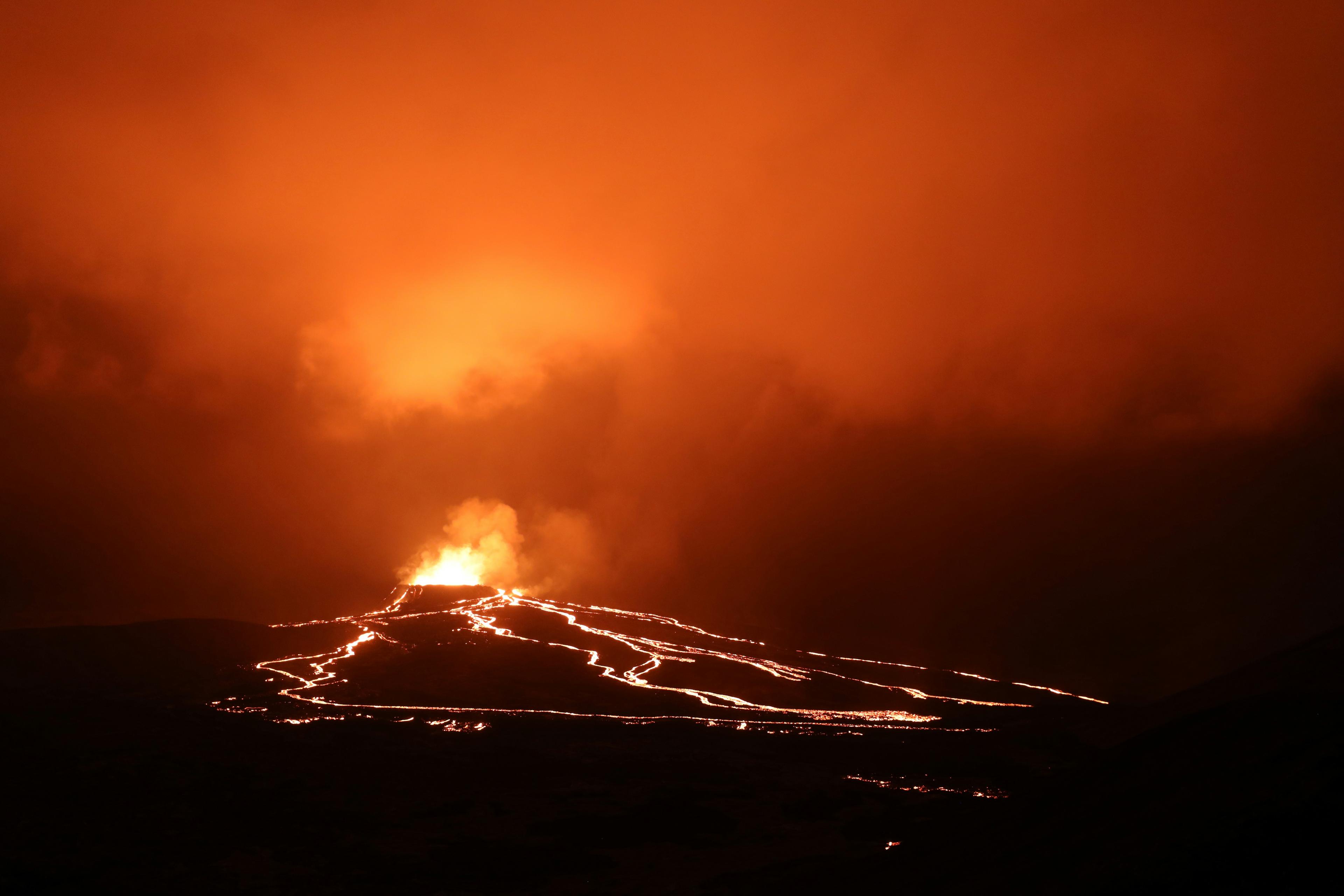 Nighttime spectacle of the Fagradalsfjall eruption, with glowing lava streams etching fiery paths down the slopes, all under a dramatic, glowing sky.