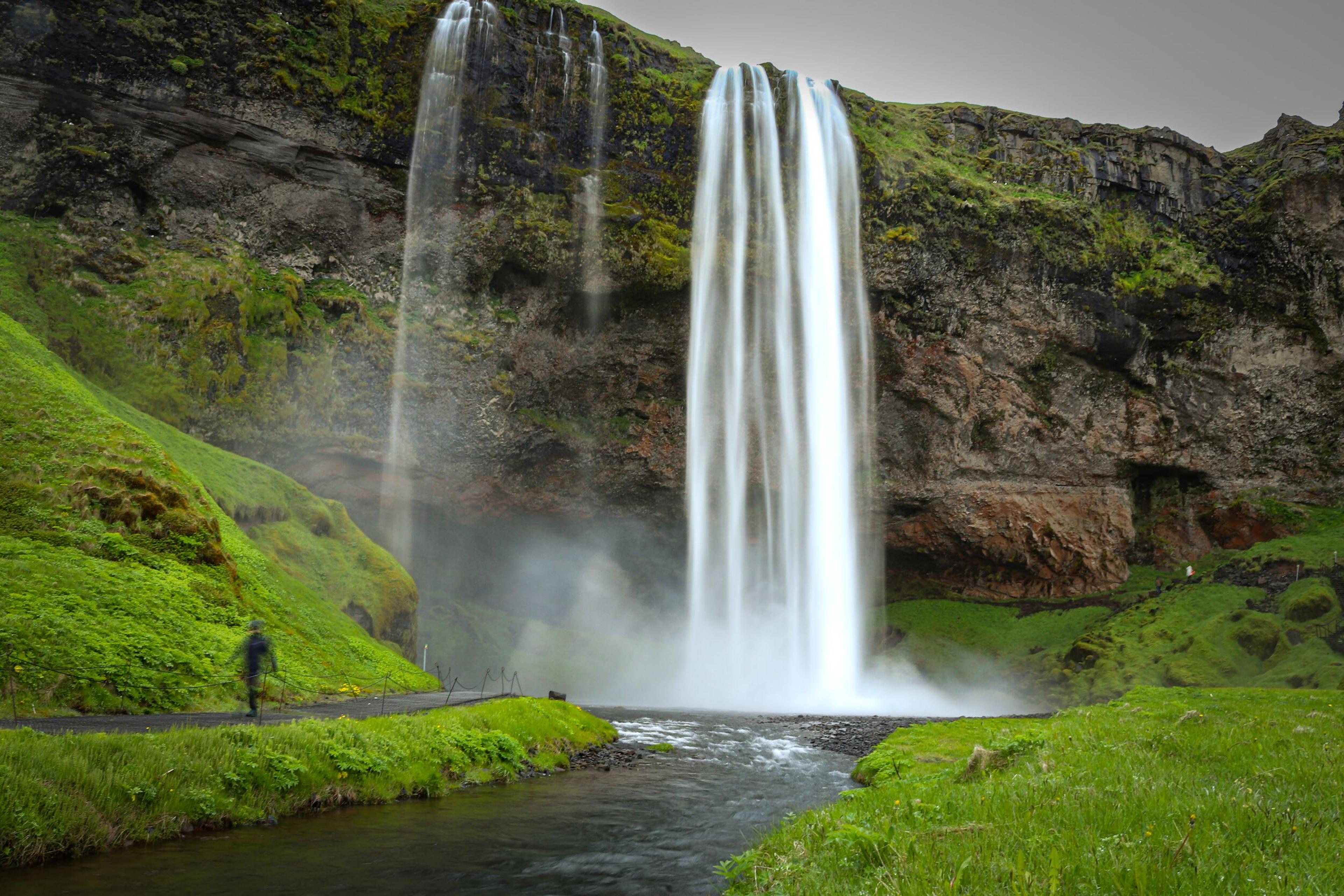 Seljalandsfoss waterfall cascading down a green, rocky cliff with a person on a nearby path.