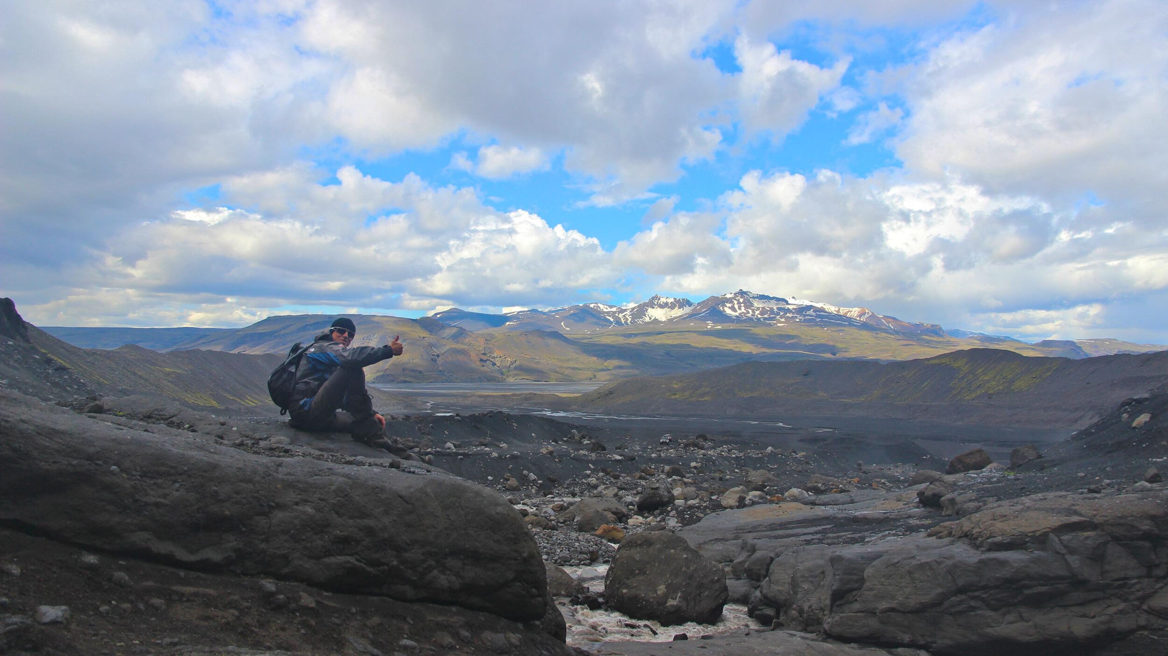 explorer sitting by a river bank, Tindfjöll Mountain on the background.