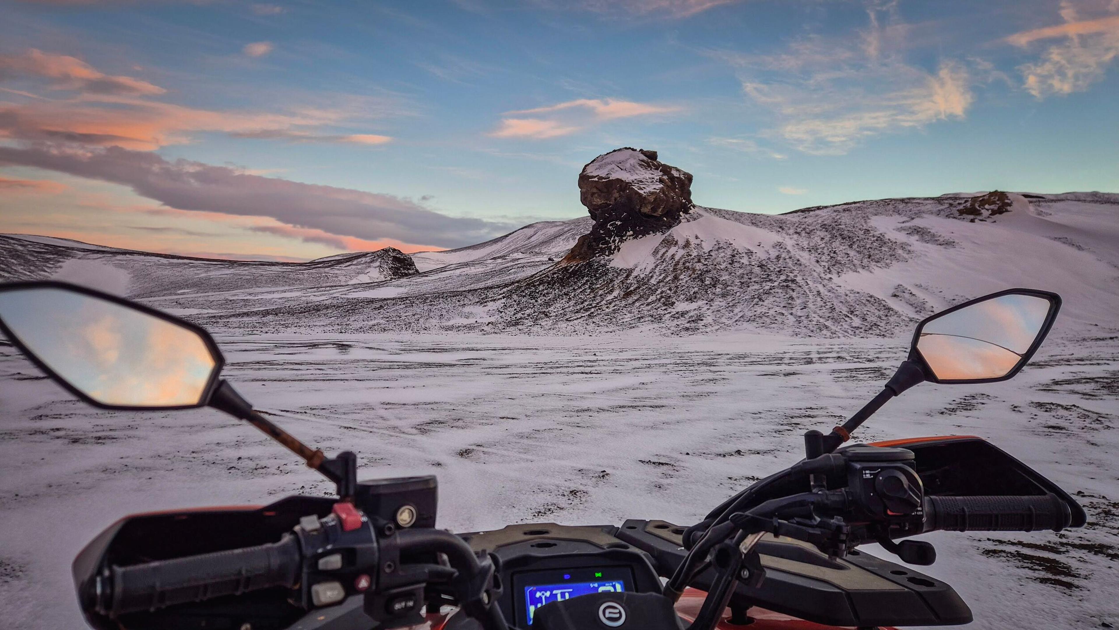 POV from an ATV in a snowy, rocky landscape at sunset.