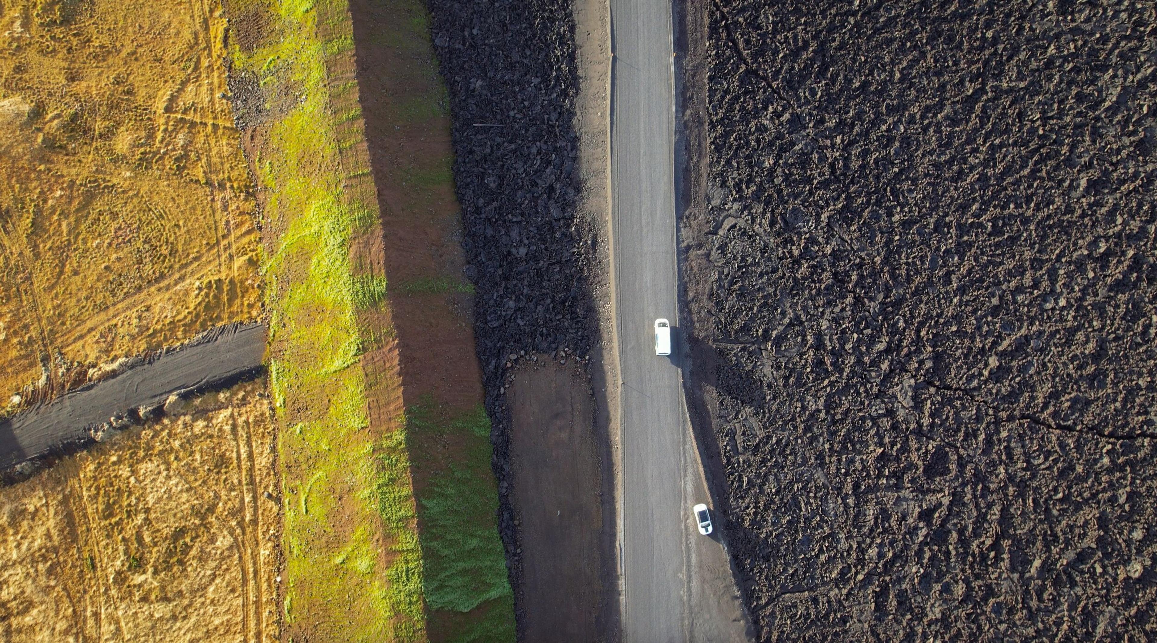 an aerial view of a car driving down a road between two fields .