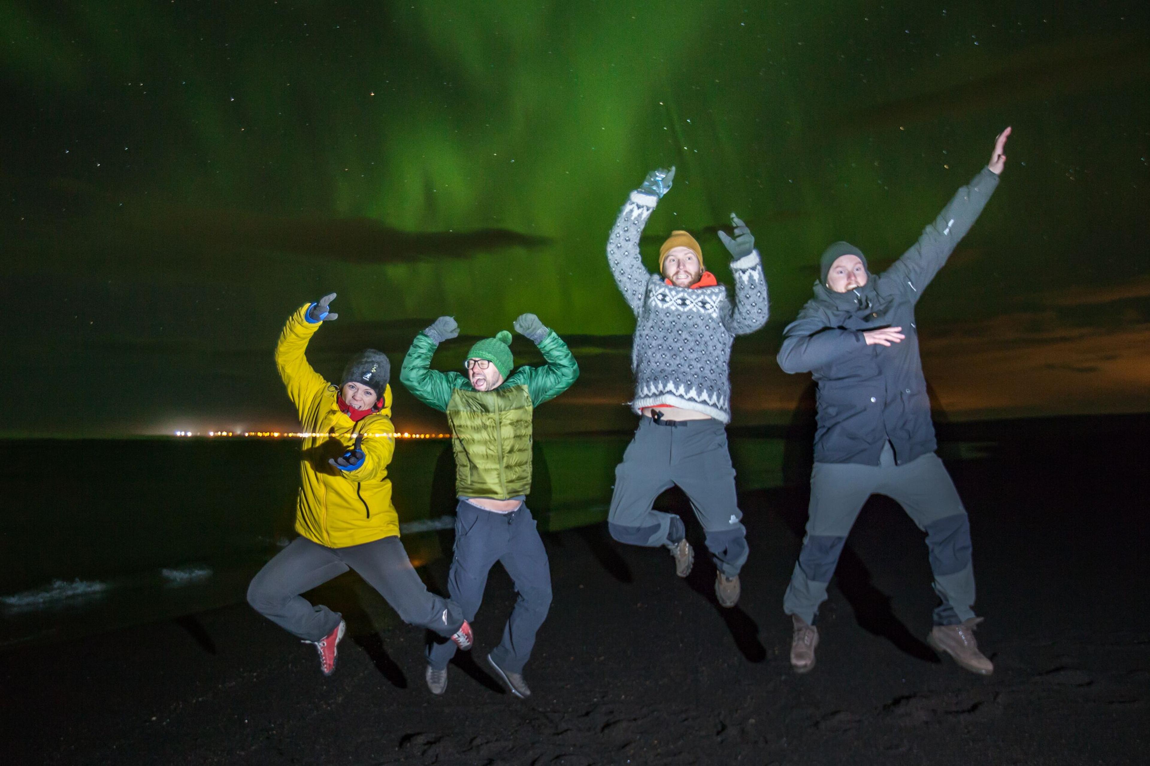 Joyful travelers leaping in the air, posing for a photo with the mesmerizing Northern Lights illuminating the night sky.