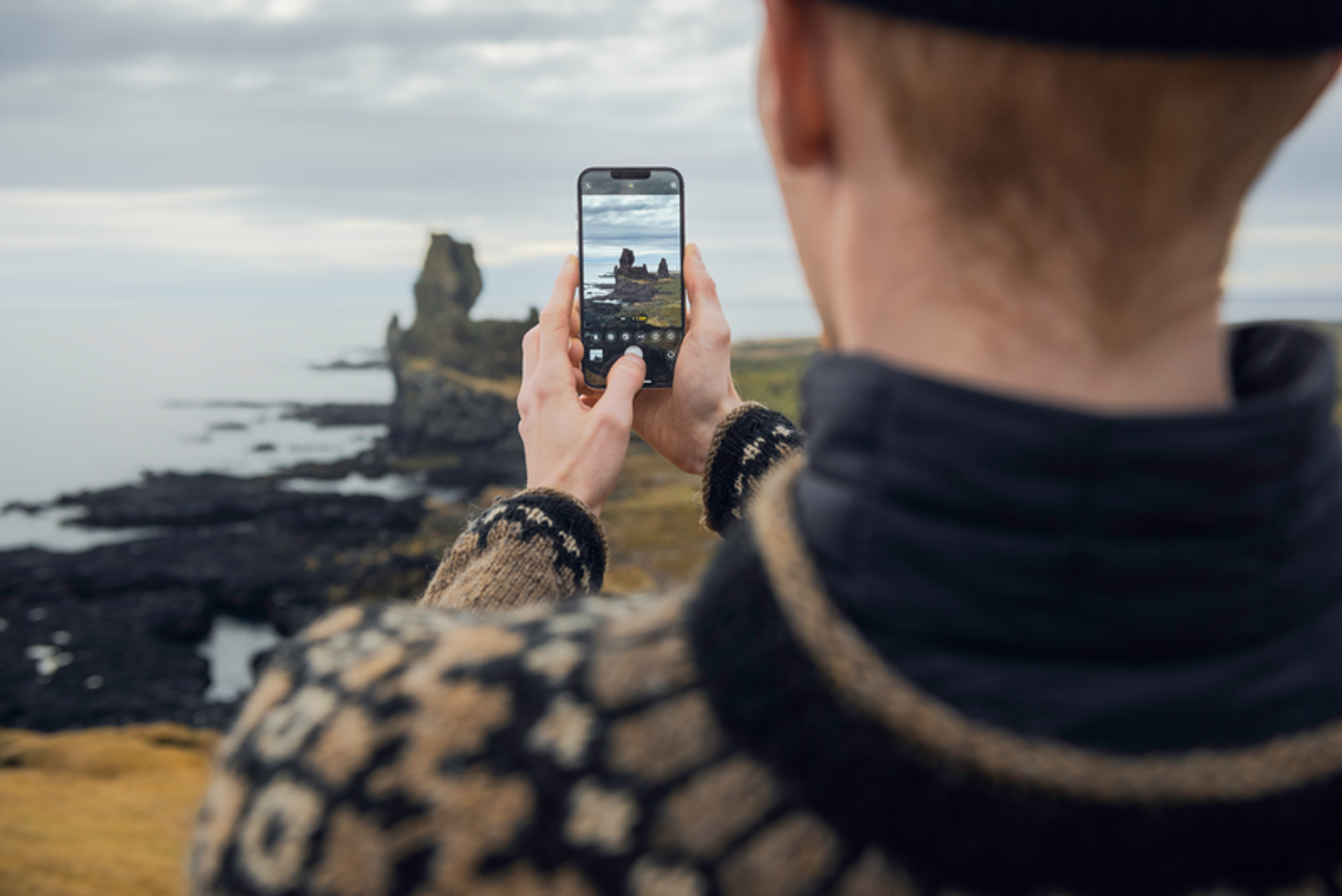 A person wearing knitted sweater taking a photo of a coastal rock formation