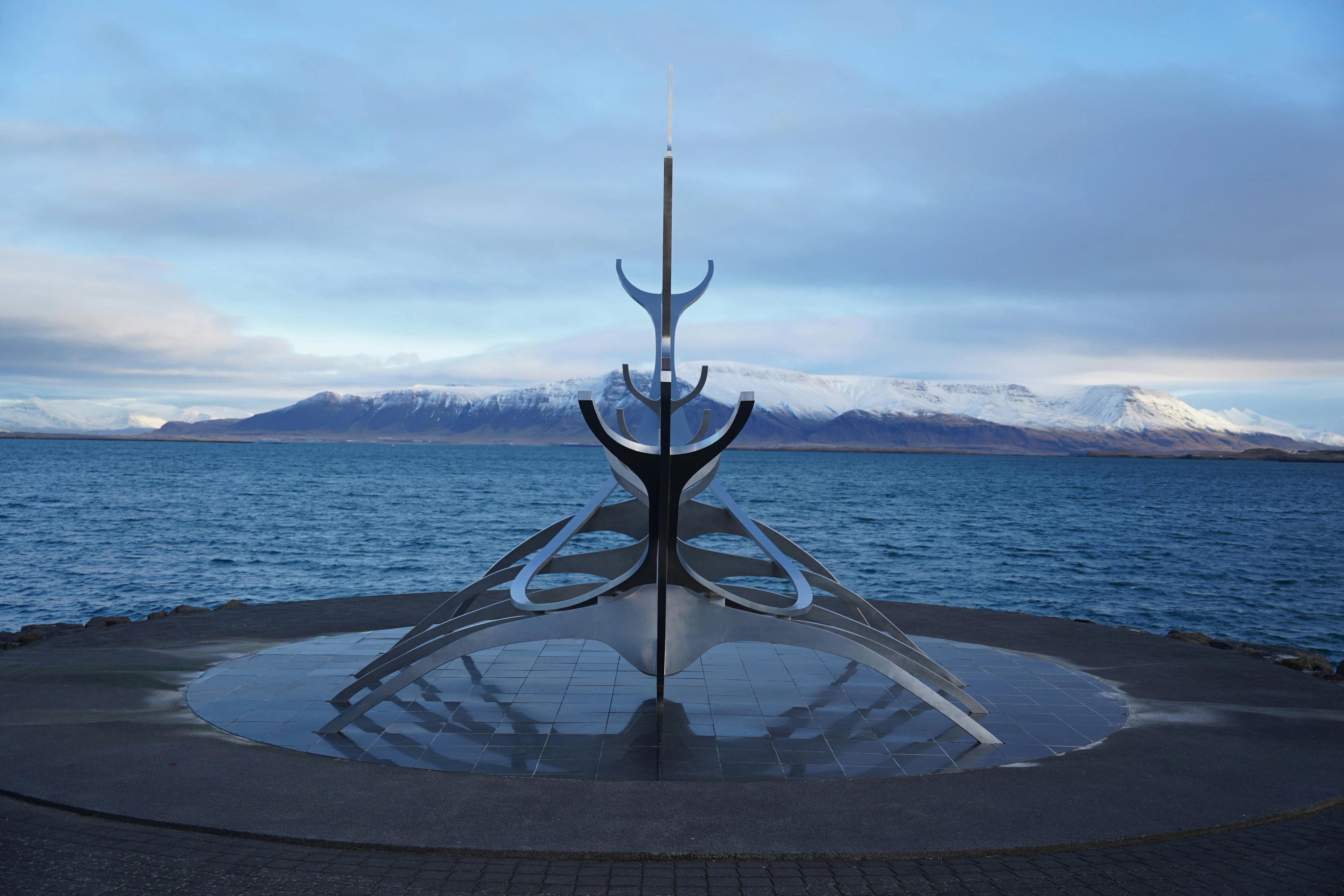 The Sun Voyager sculpture, an abstract metal ship, on a waterfront with a bay and snow-capped mountains in the background.