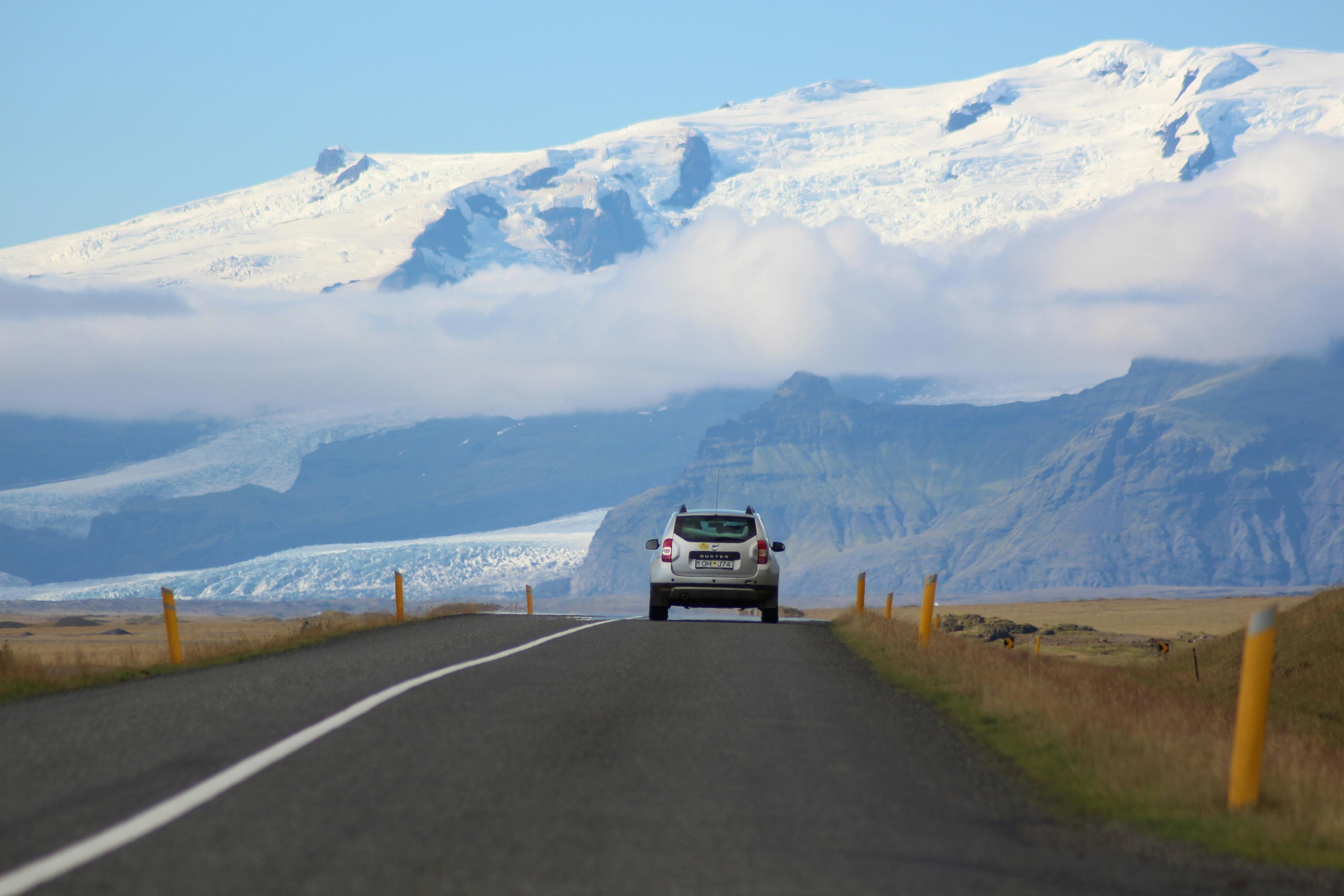 A car heading towards a glacier-capped mountain