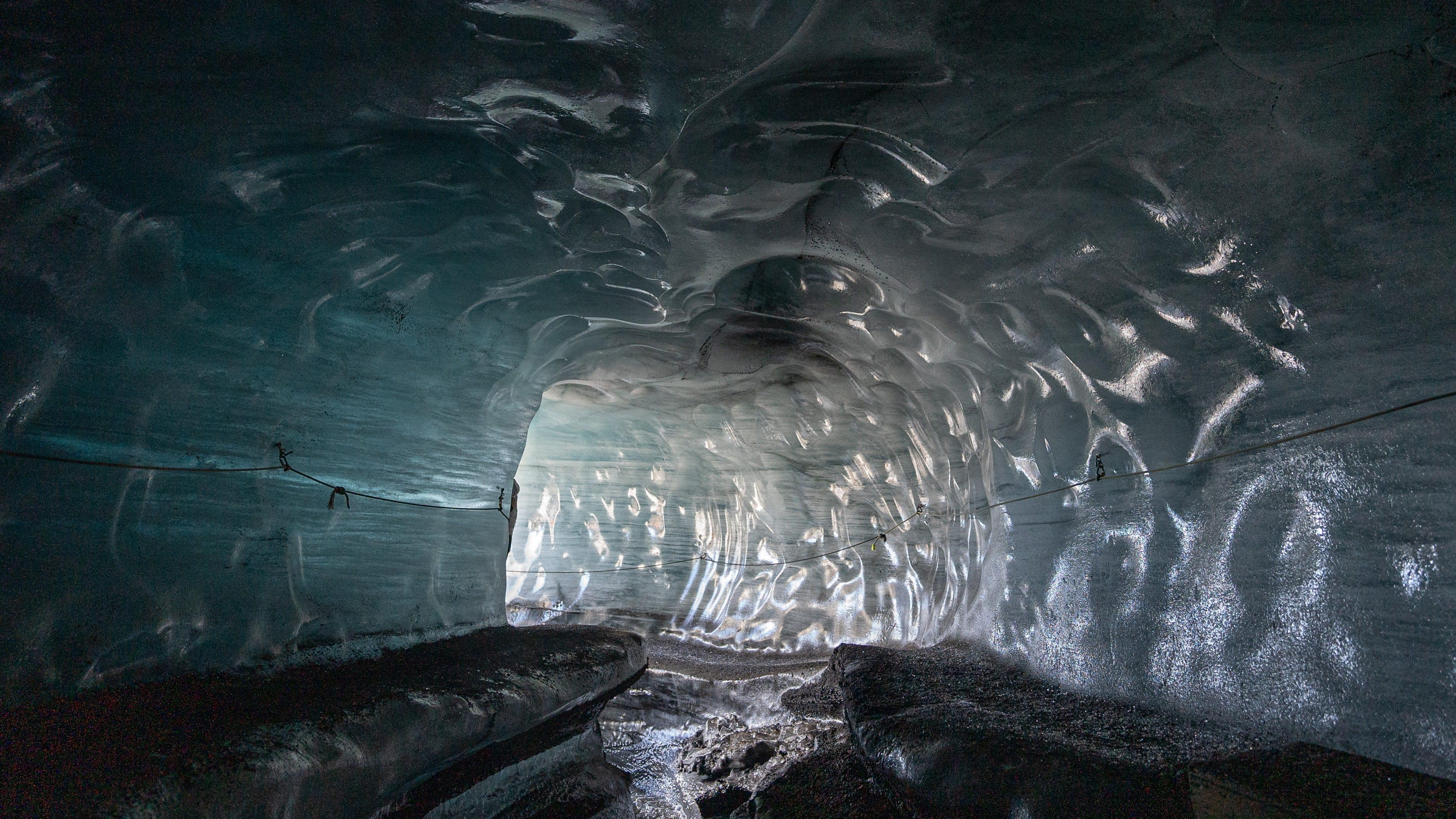 Inside a shimmering blue ice cave tunnel with a bright opening ahead.