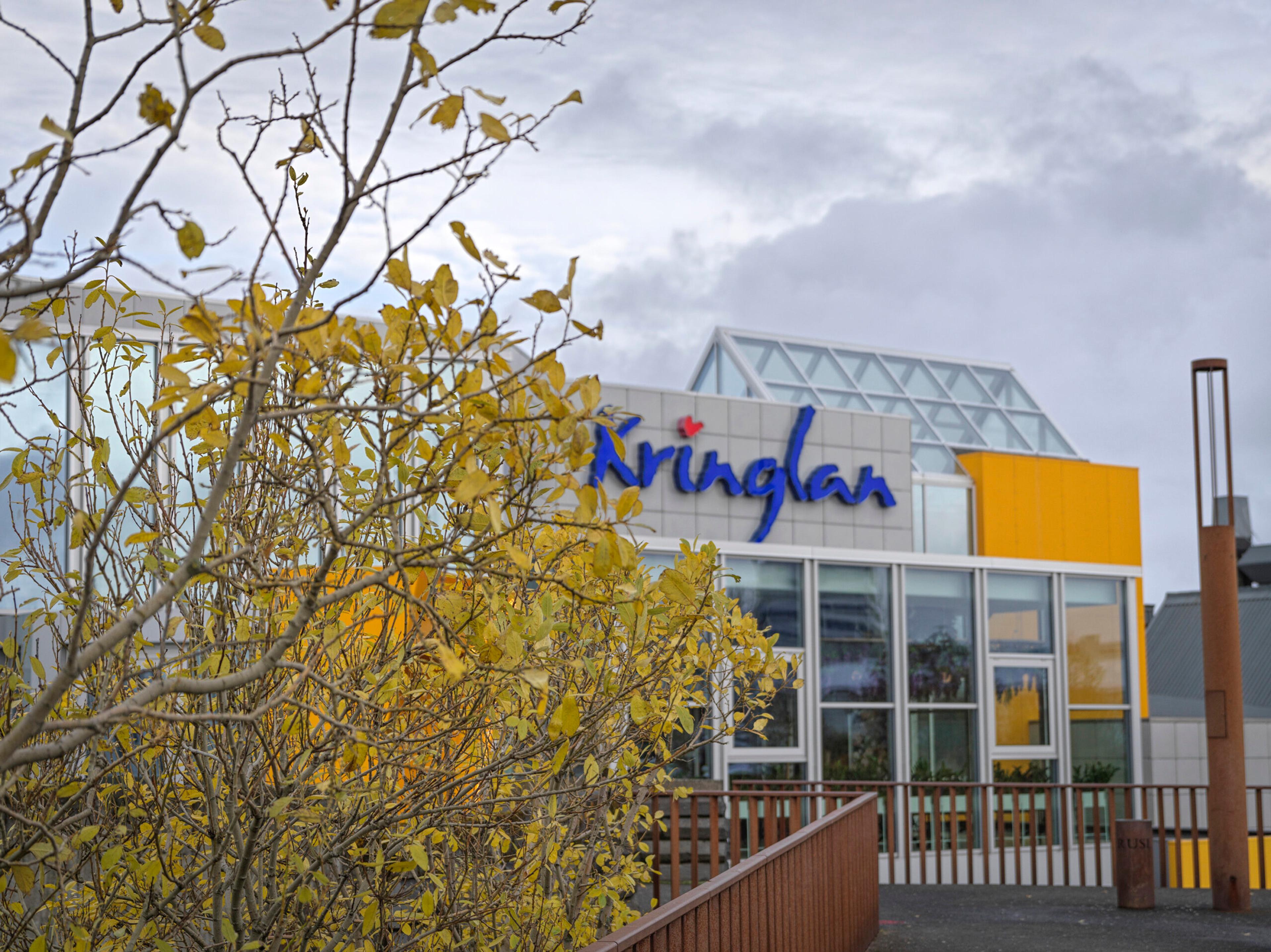 Exterior of Kringlan shopping mall with its colorful facade and autumn leaves in the foreground.