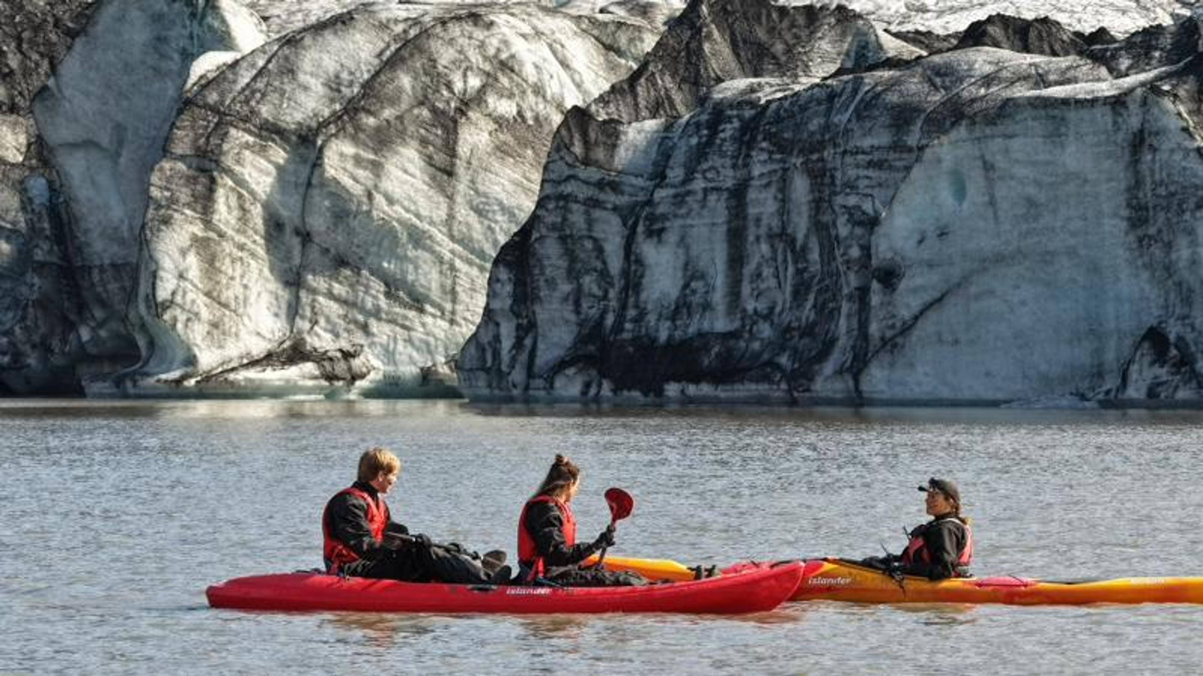 Three people kayaking on a glacial lake.