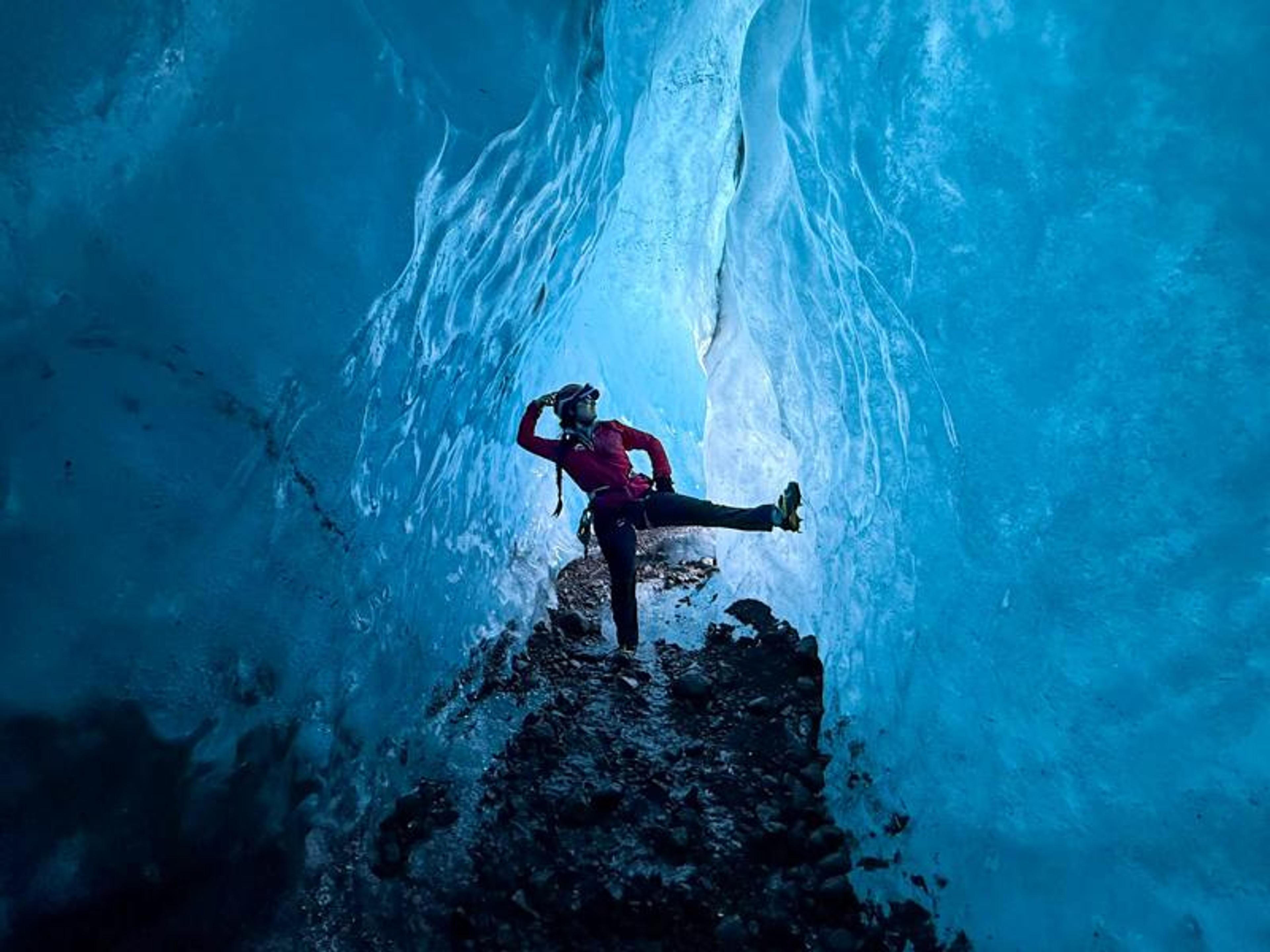 A person poses inside a glowing blue ice cave.