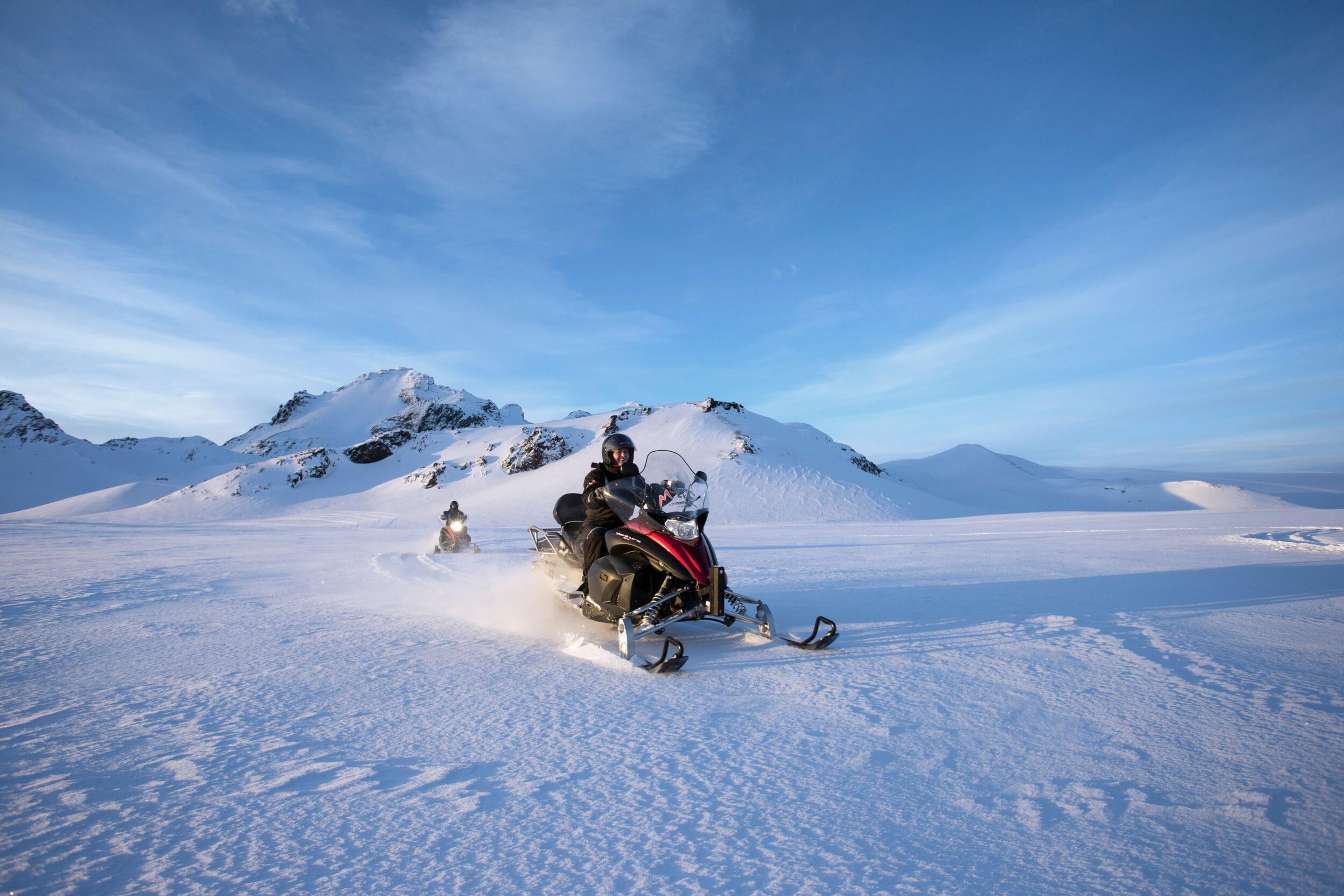 Snowmobilers enjoying a sunny day on a snowy mountain.