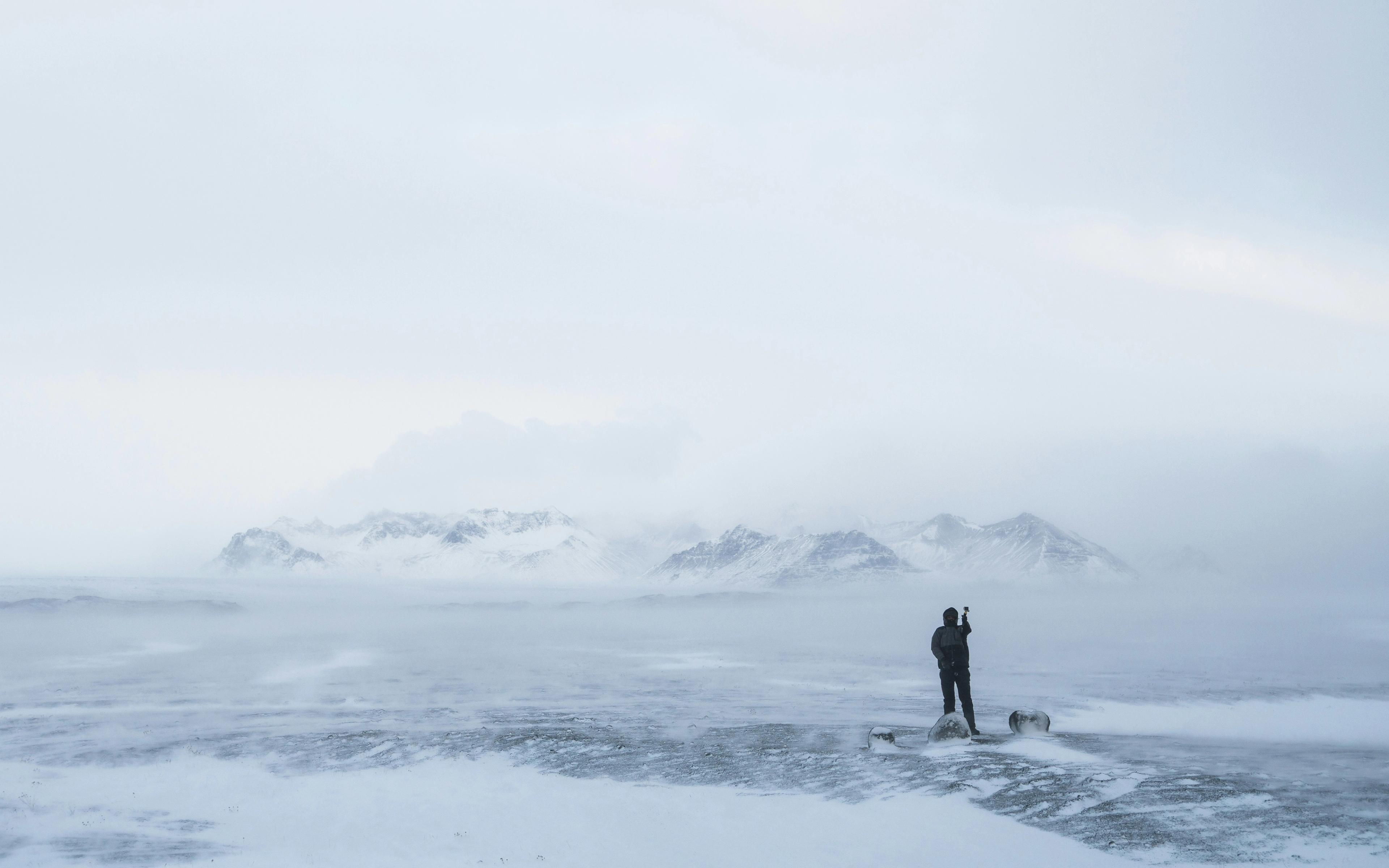 A lone figure stands on an icy plain with mountains shrouded in fog.