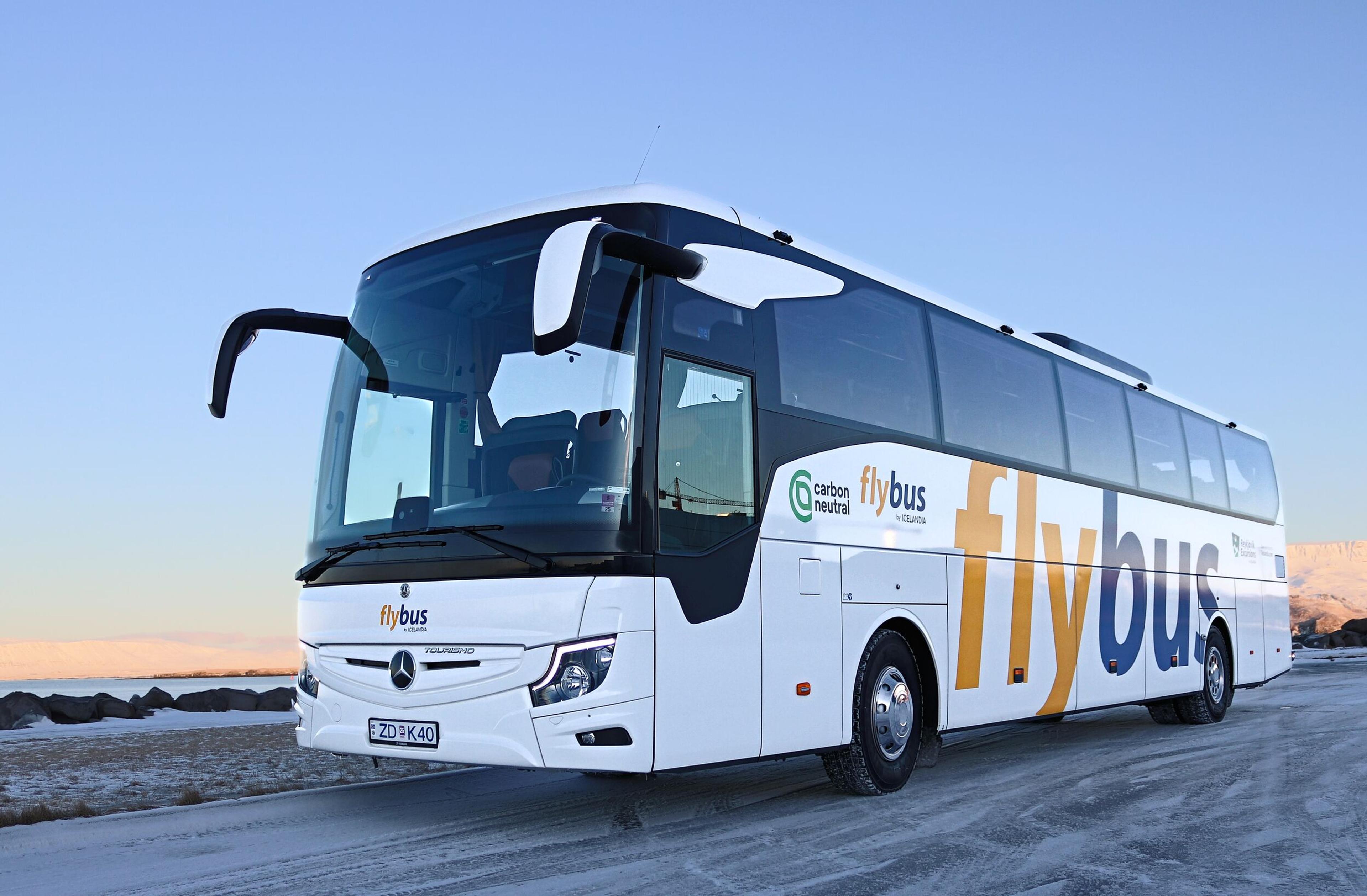 A white Flybus coach bus with "carbon neutral" branding on a snowy road and a distant winter landscape.