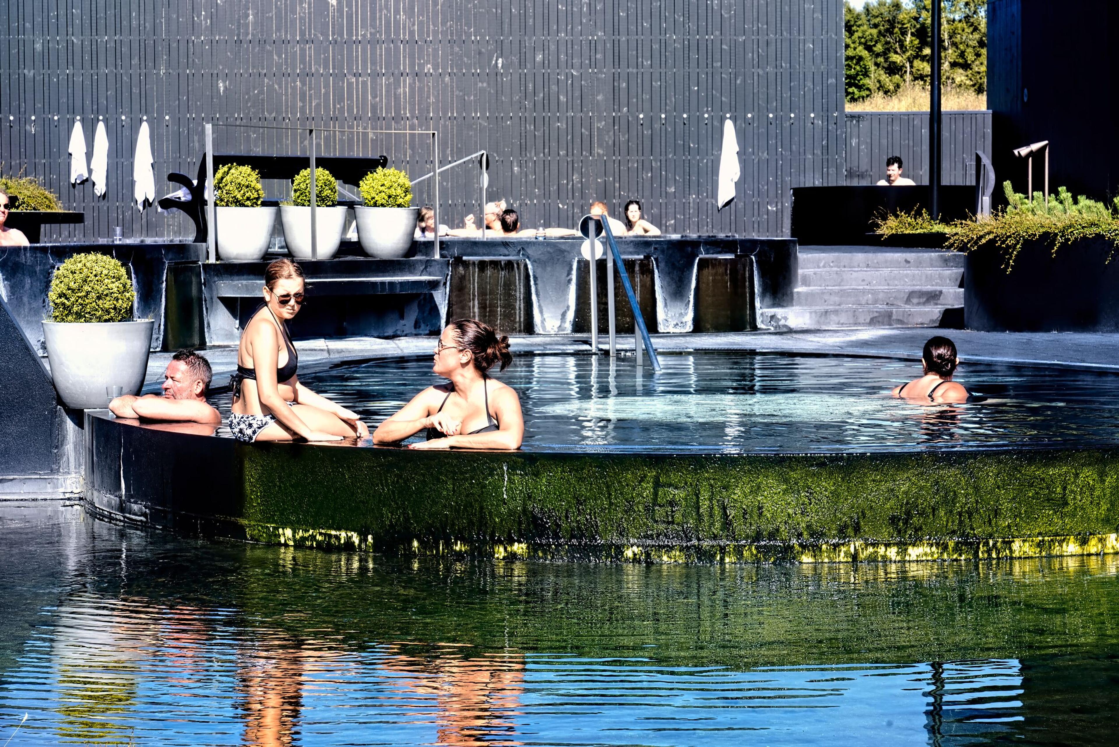 Visitors enjoying the warm geothermal pools at Krauma Geothermal Baths on Iceland's Silver Circle, surrounded by sleek black architecture, greenery, and a peaceful spa atmosphere.