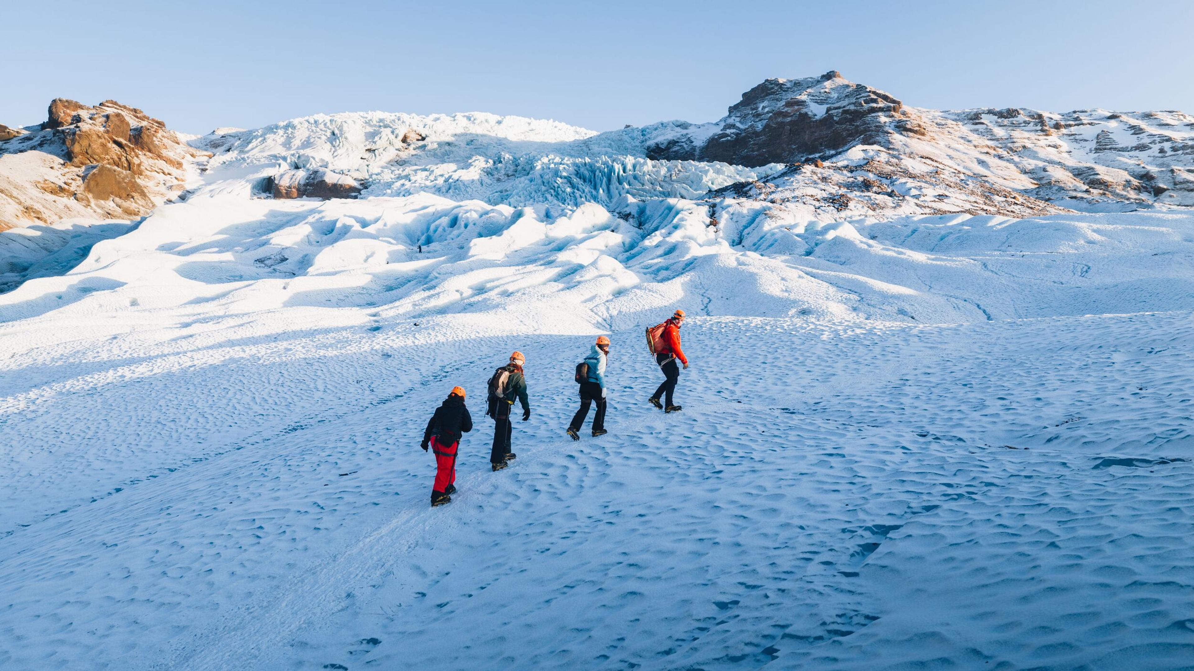 Four people hiking on a snowy glacier with mountains in the background.