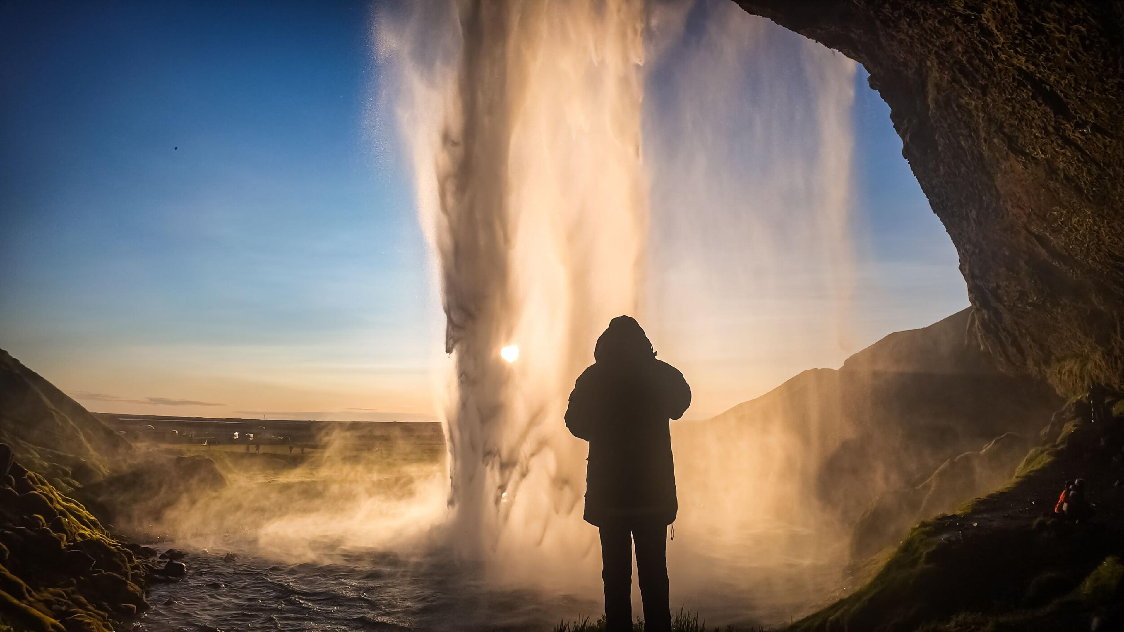 Back of a person watching a golden waterfall from inside a cave.