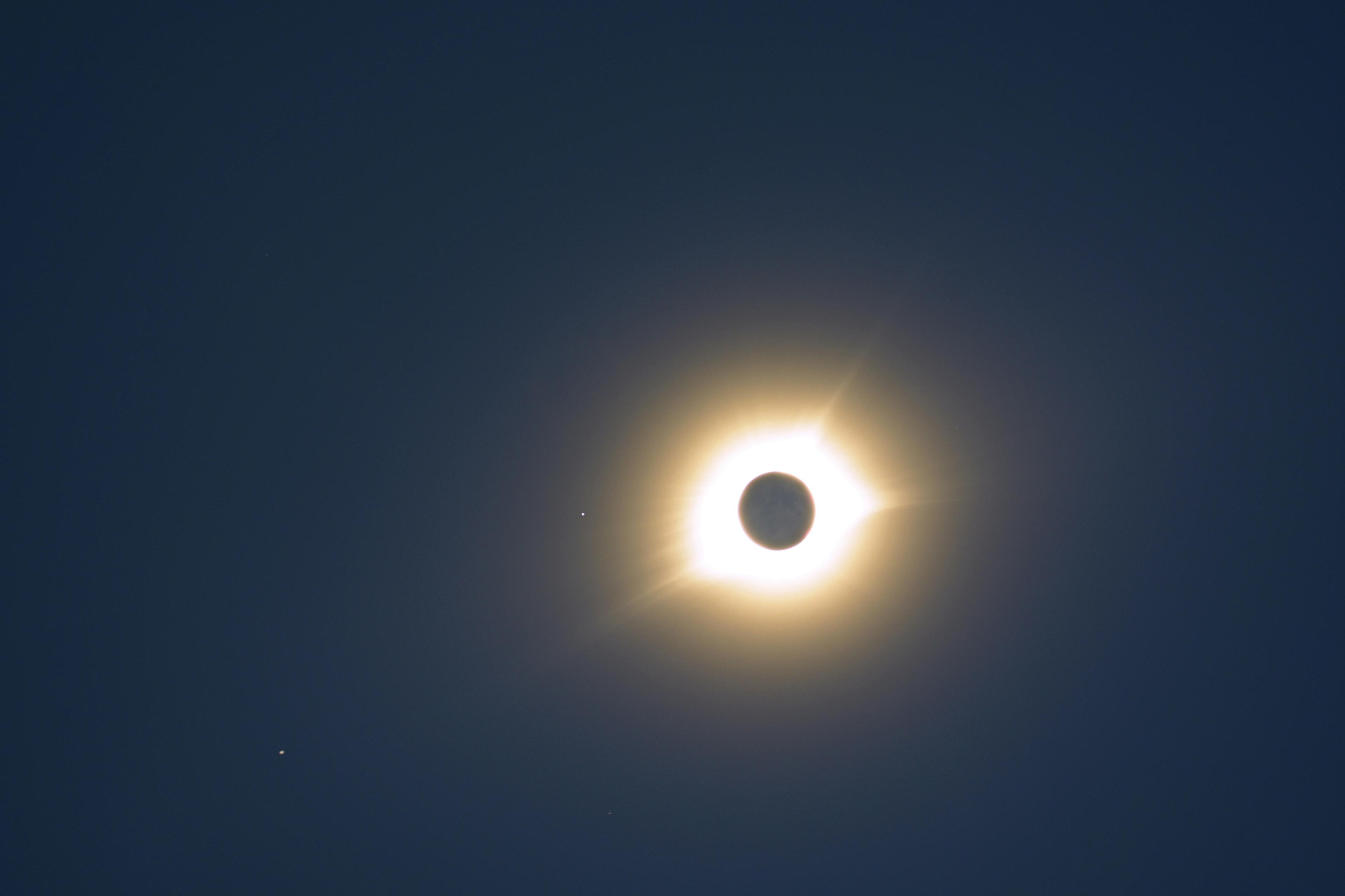 Image of a total solar eclipse, showing the dark silhouette of the moon completely covering the sun, with the bright solar corona glowing around it against a dark sky.