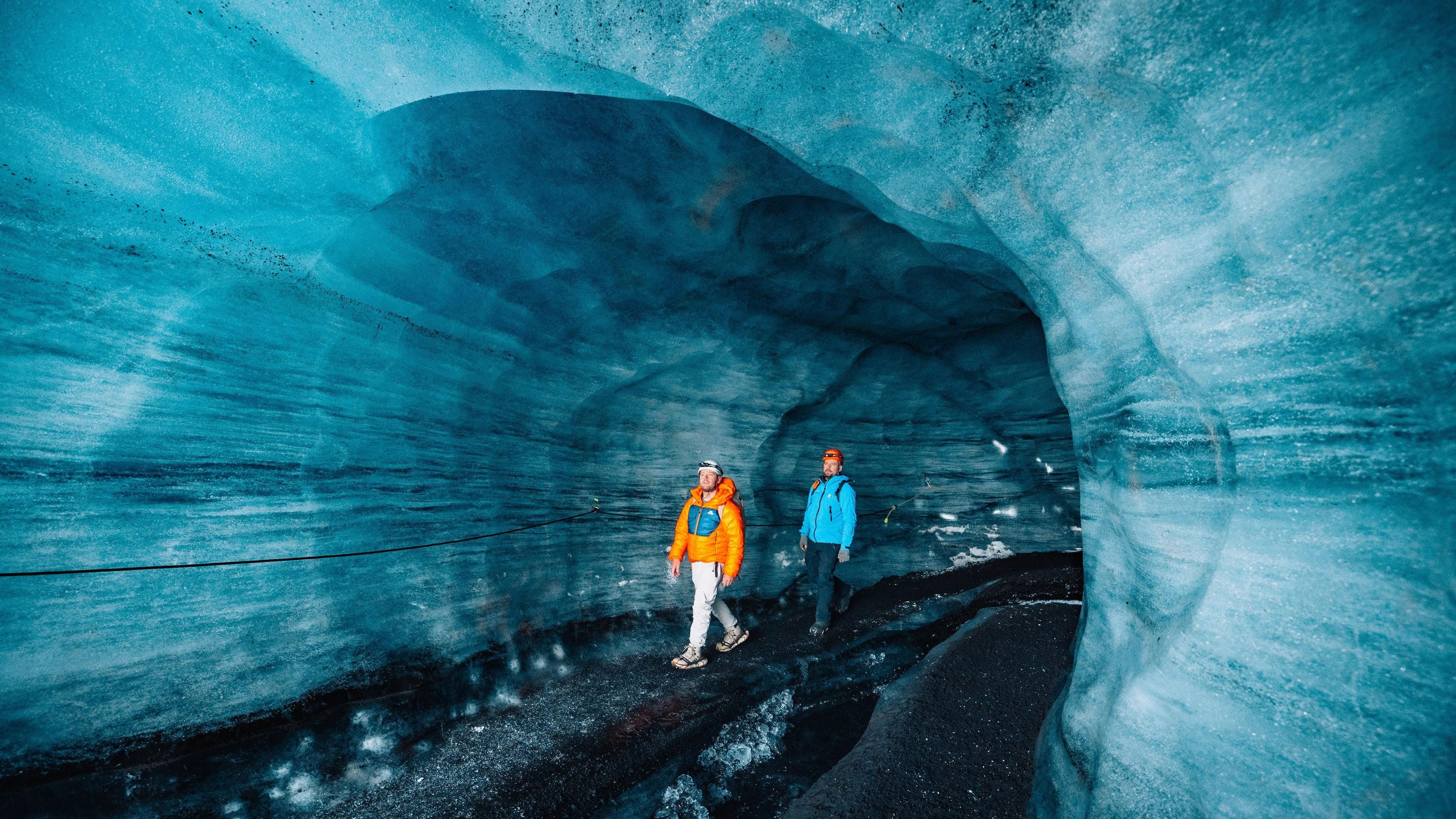 Two people walk through a vibrant blue ice cave.