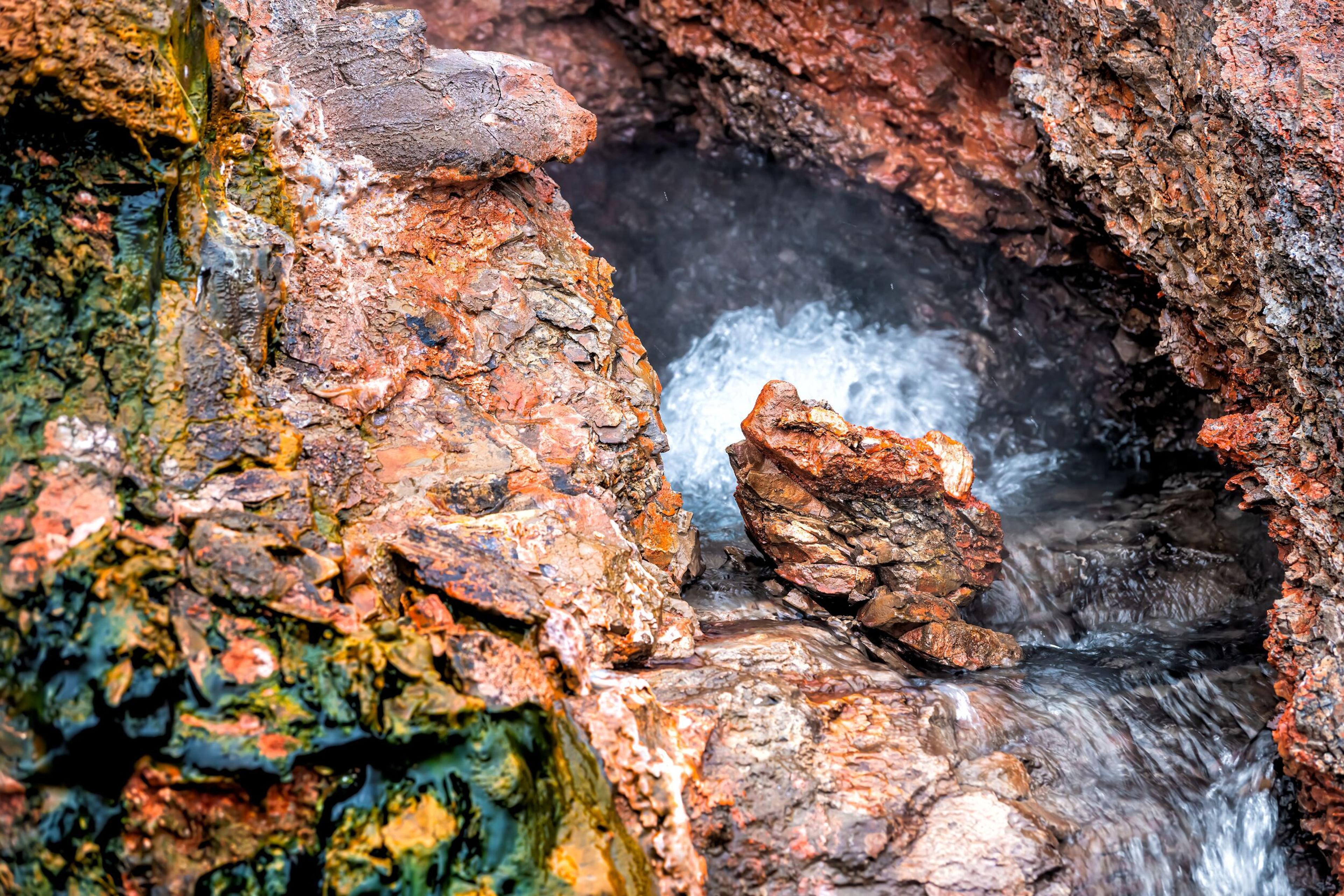 Close-up of vibrant, mineral-rich rocks surrounding a steaming geothermal spring, with water bubbling to the surface, showcasing the dynamic natural activity of a hot spring.