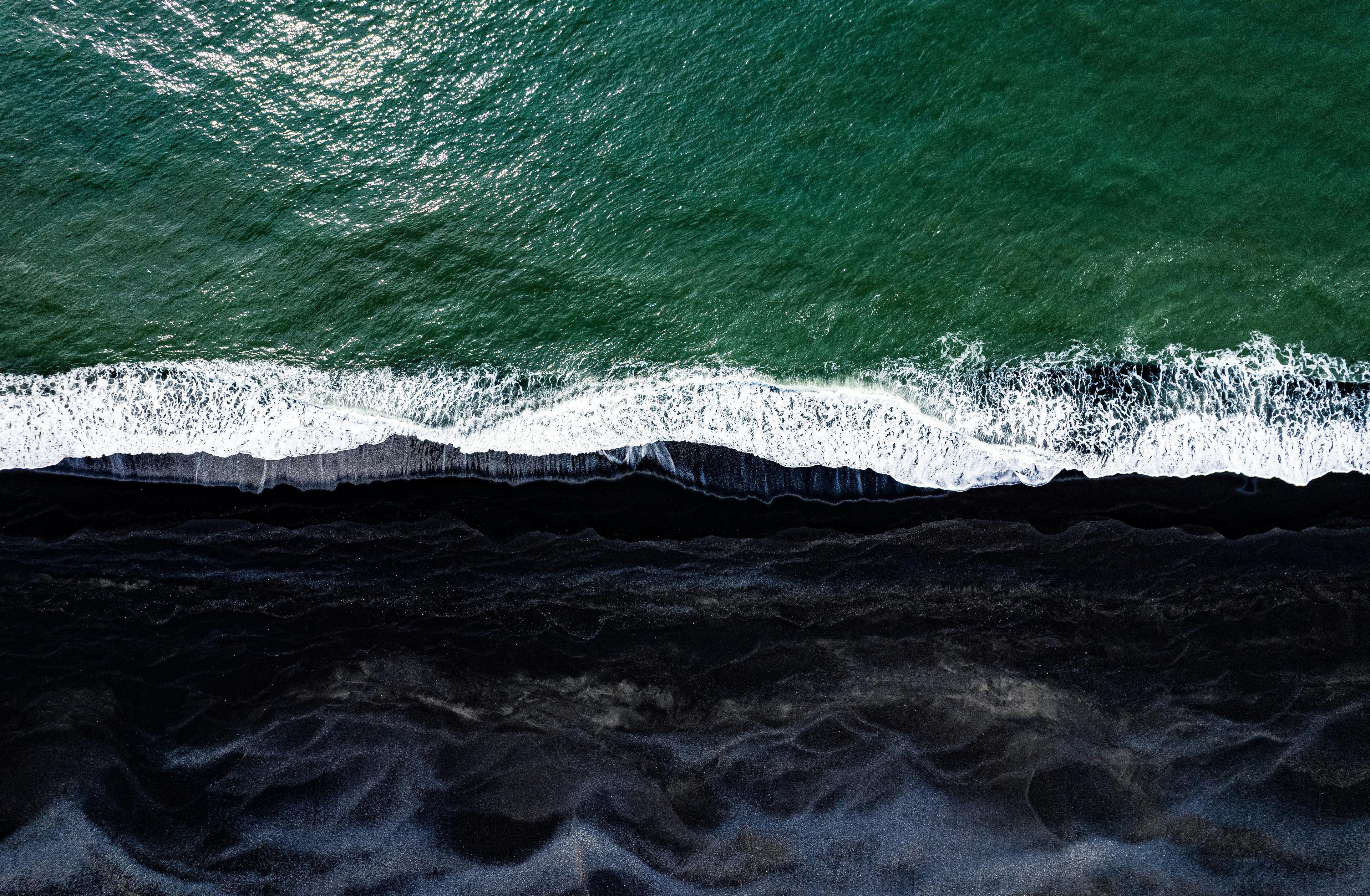 Aerial view of the black sand beach in Vík, where the dark sand meets the green waves of the ocean.