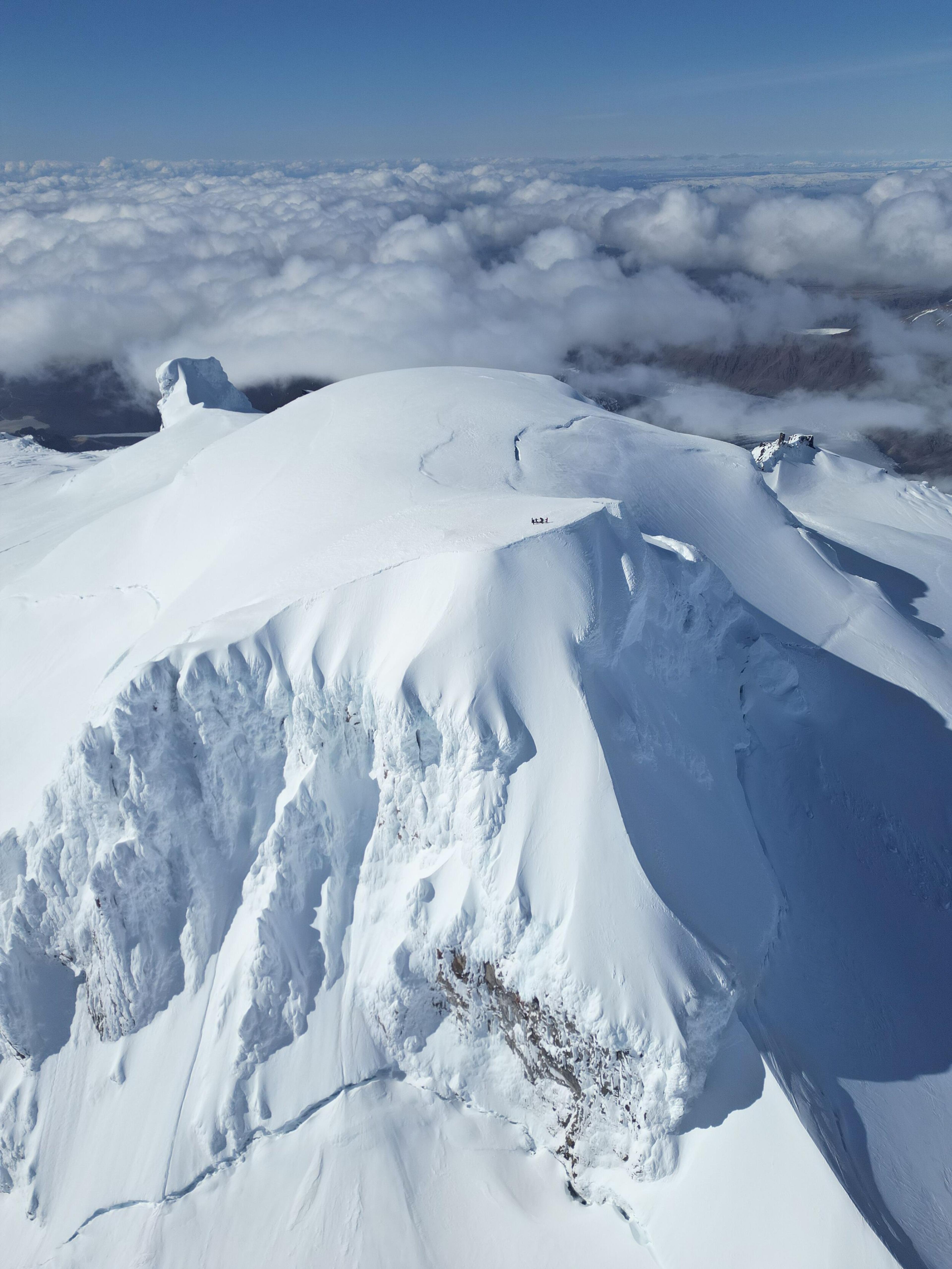 Snowy mountain summit with climbers above a sea of clouds.