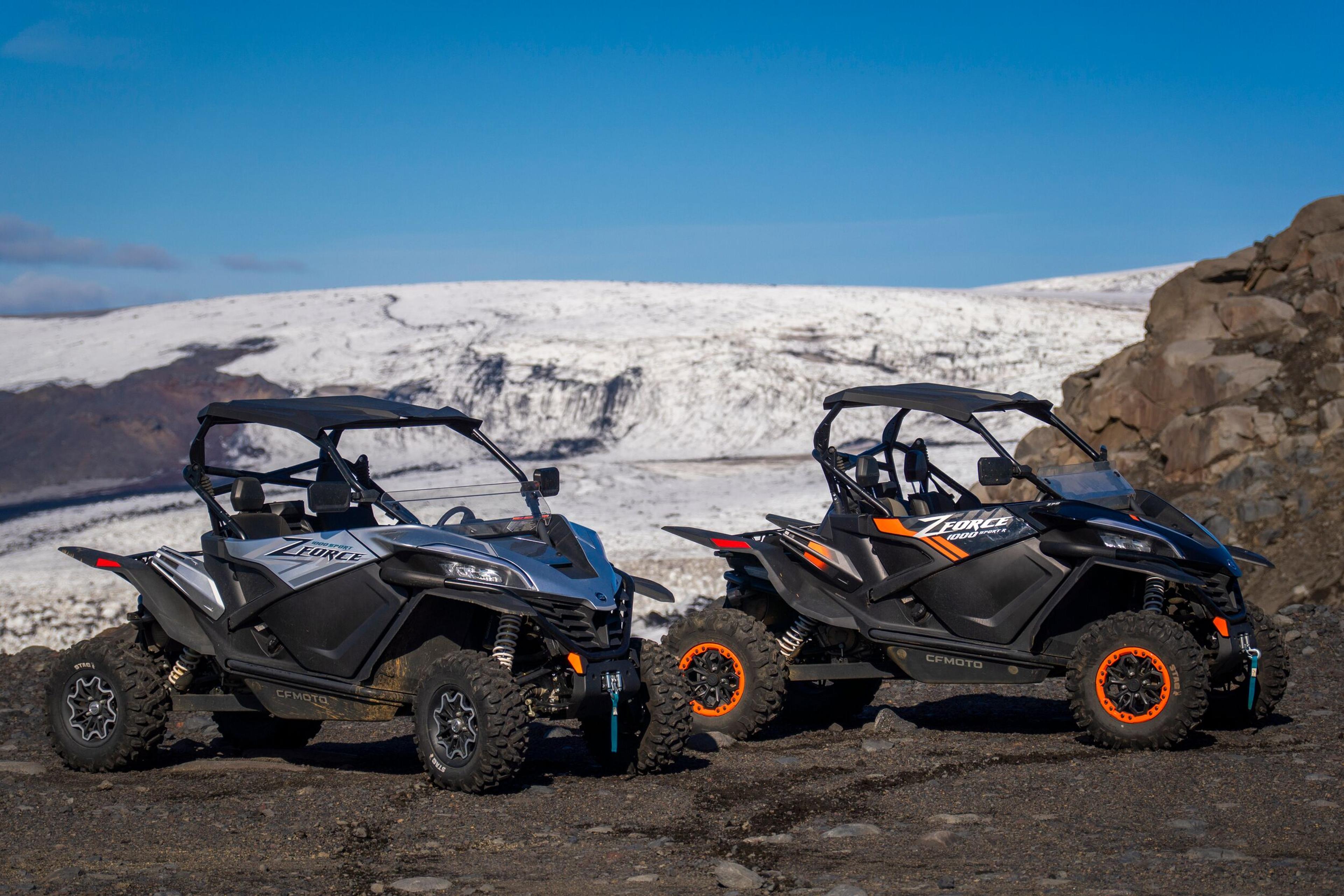 Two off-road buggies with prominent orange rims parked on rocky terrain with a backdrop of a glacier, likely part of a glacier buggy tour in Iceland.