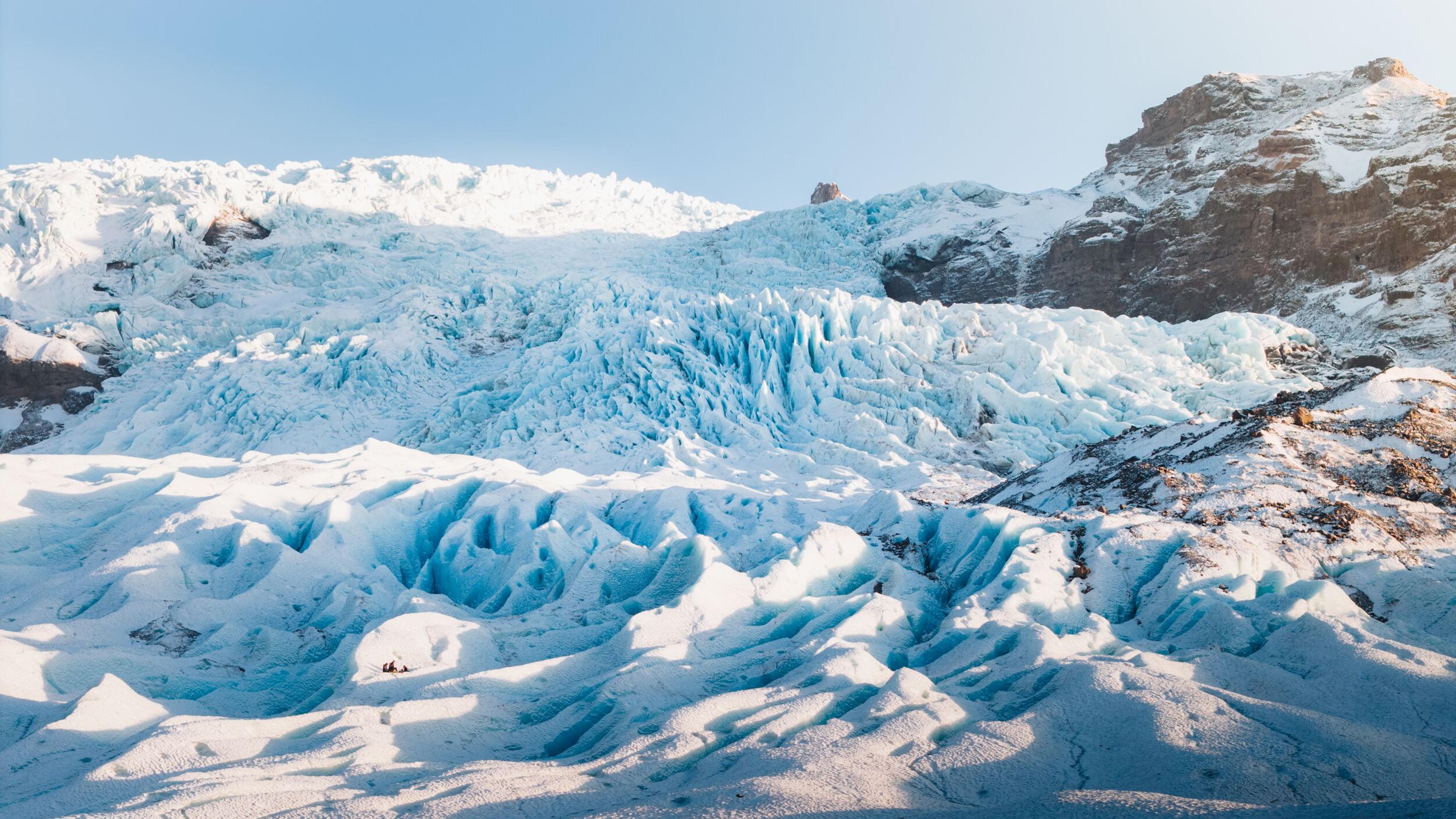 A large glacier with prominent blue ice and snow-covered mountains.