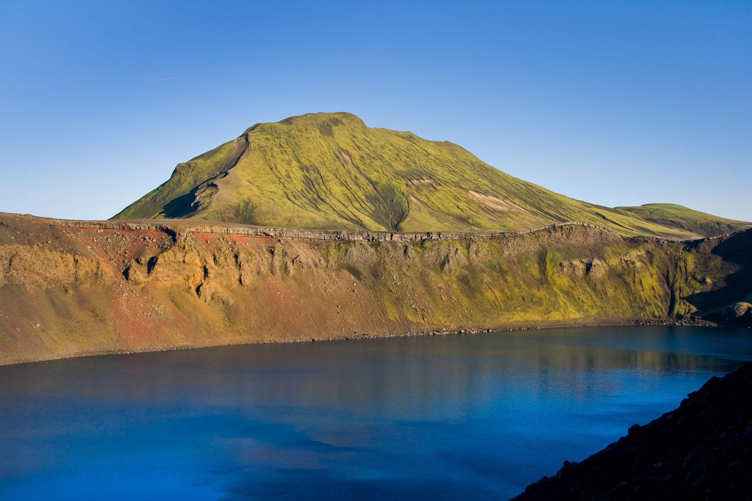 A scenic view of Ljótipollur crater in Landmannalaugar, Iceland, featuring a deep blue lake nestled within the crater's steep, multicolored walls.