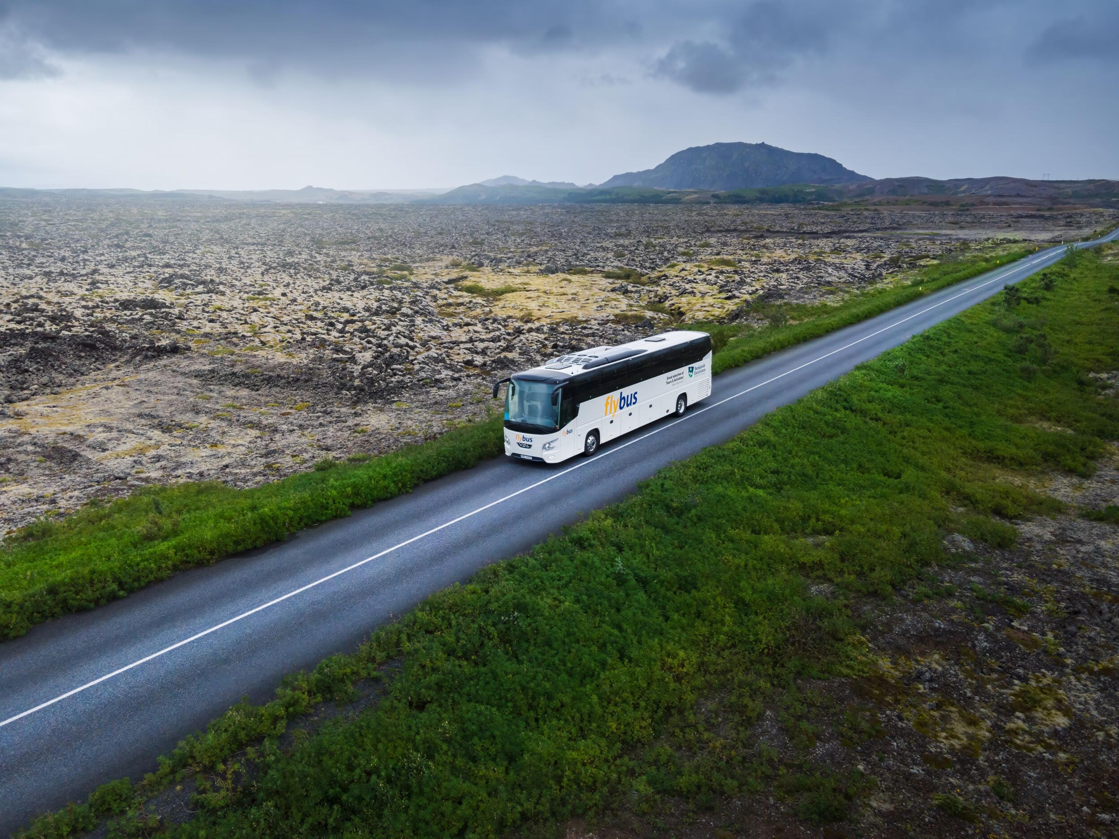 A white bus labeled 'Flybus' on the road amidst the Icelandic landscape