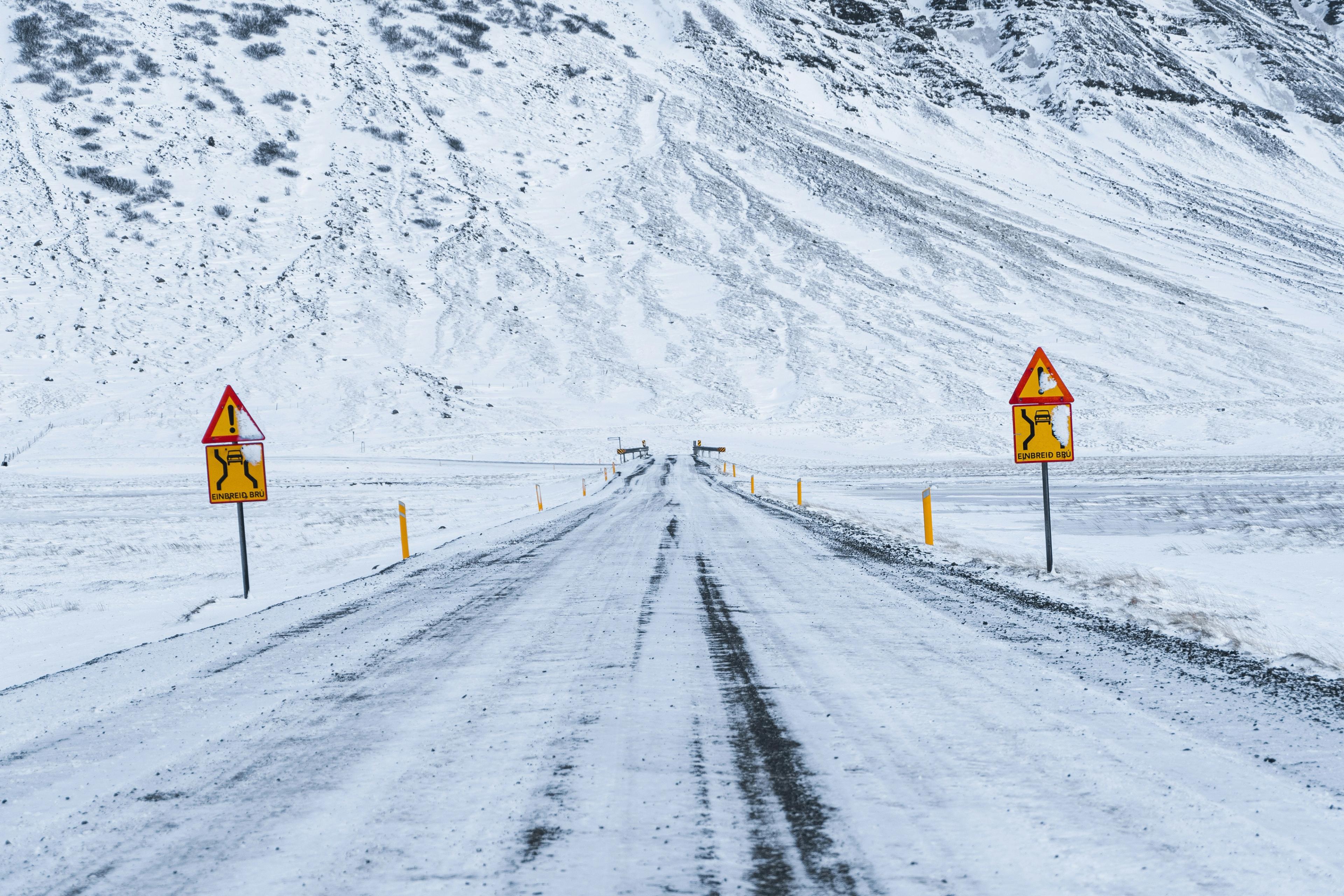 a snowy road with two yellow signs on the side of it .