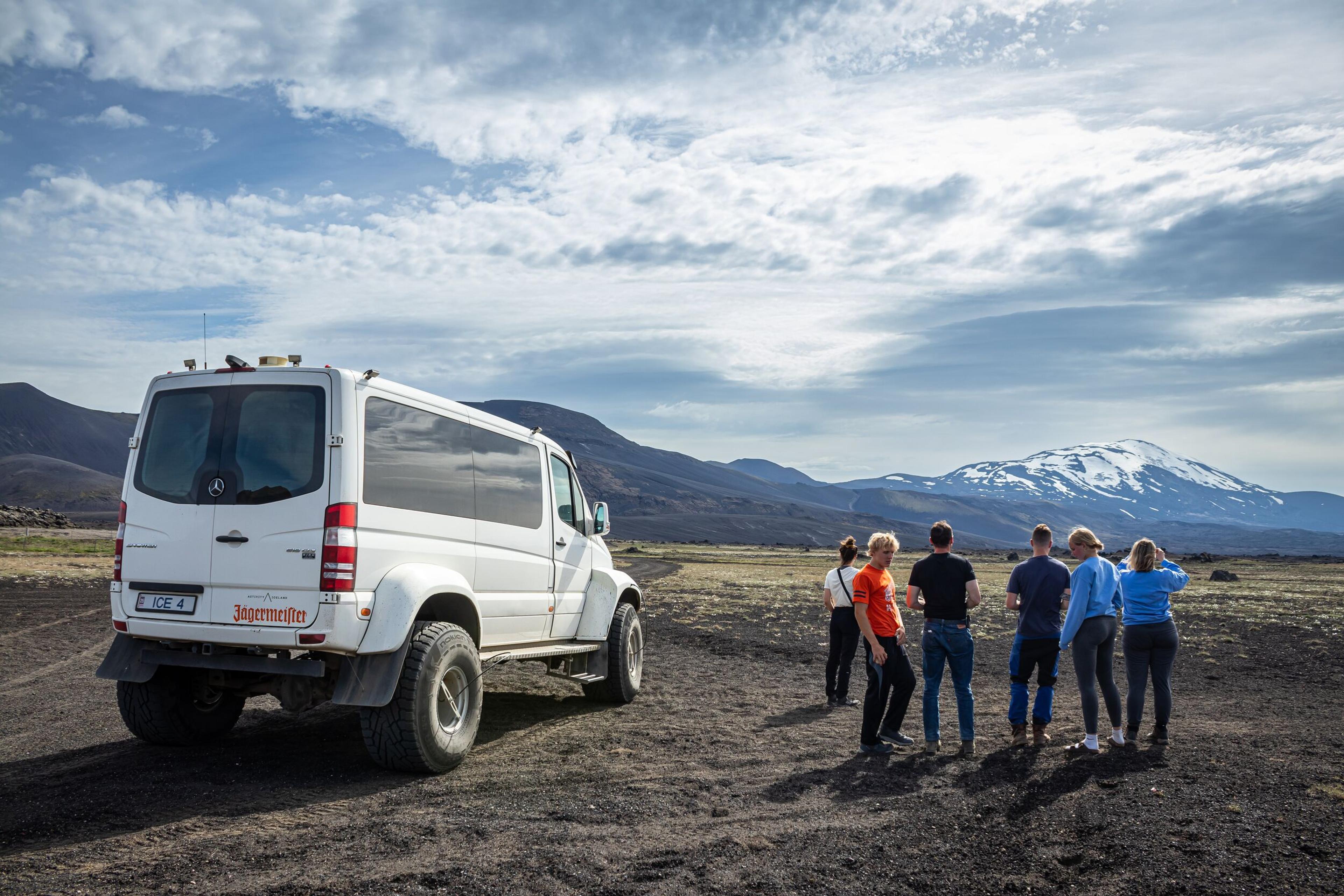 Group of tourists beside a superjeep with snow-capped mountains in the Iceland Highlands.