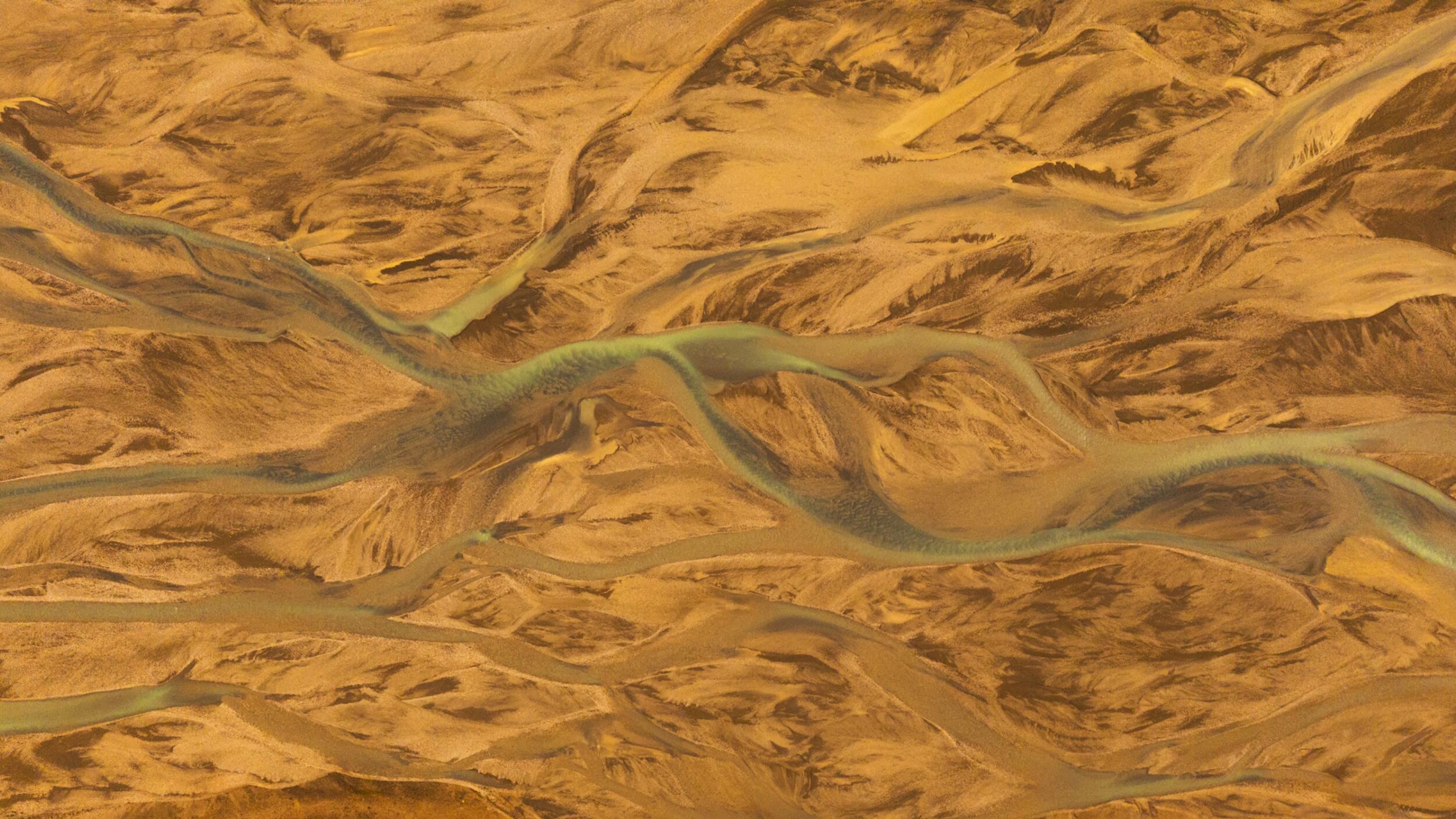 Aerial view of a braided glacial river system with turquoise water flowing through a tan, sandy landscape at Landmannalaugar.
