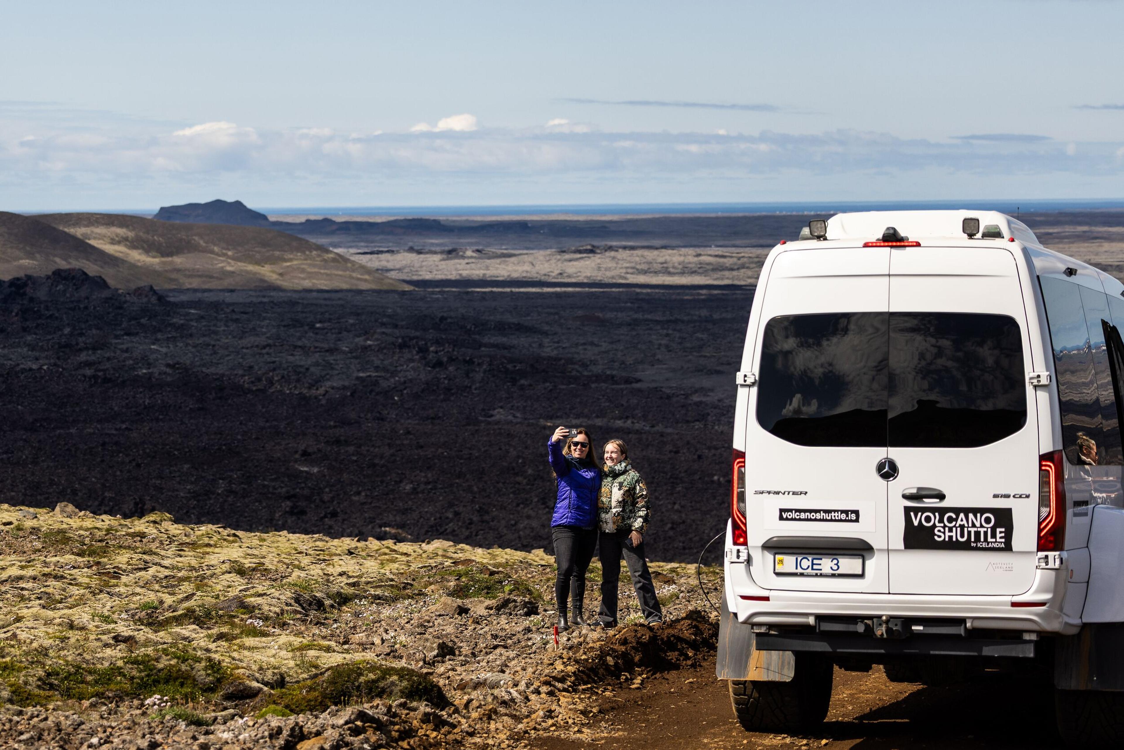 a couple of people standing next to a van on top of a hill .
