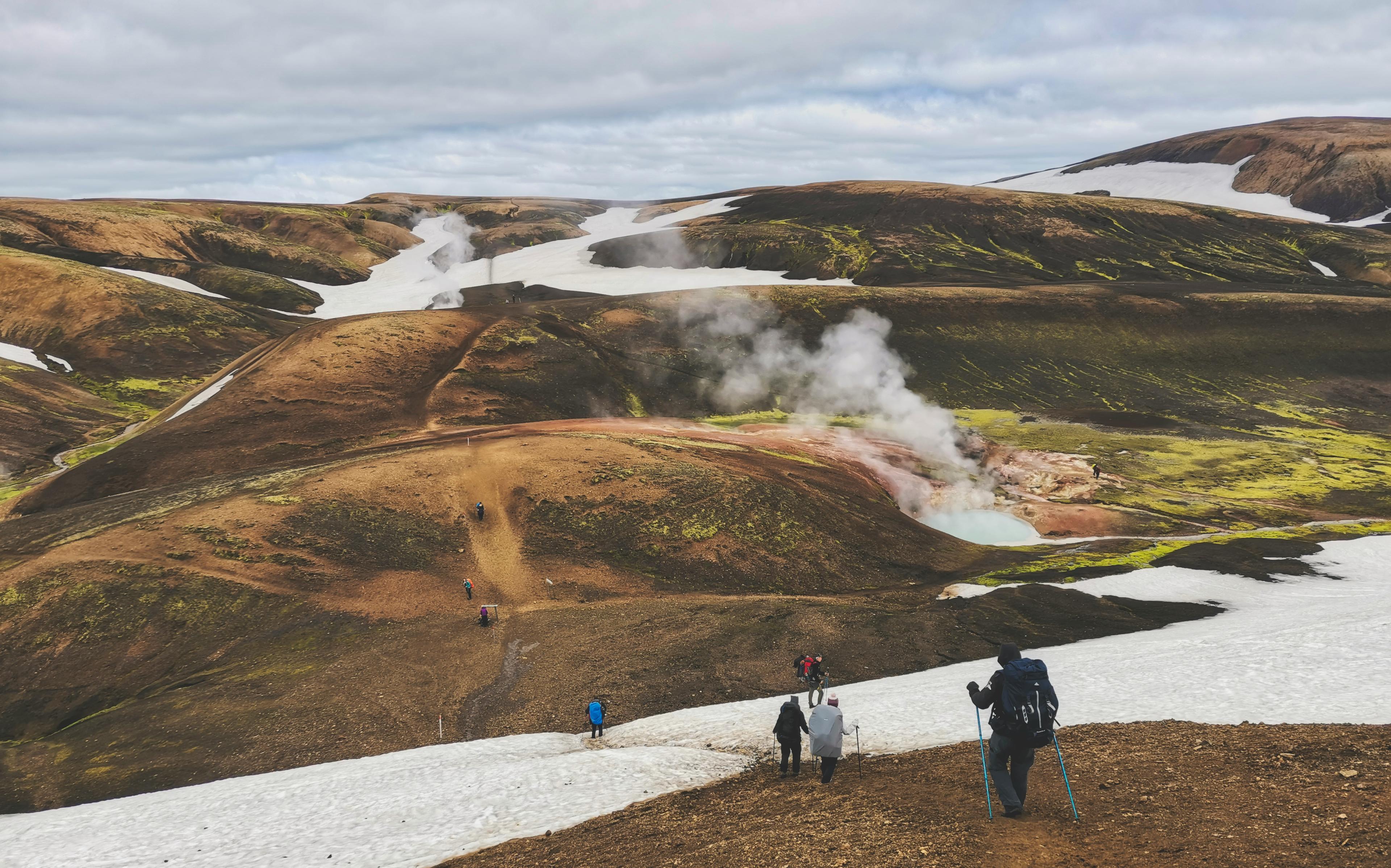 Hikers walking toward a geothermal area with steam rising from hot springs along the Laugavegur trail.