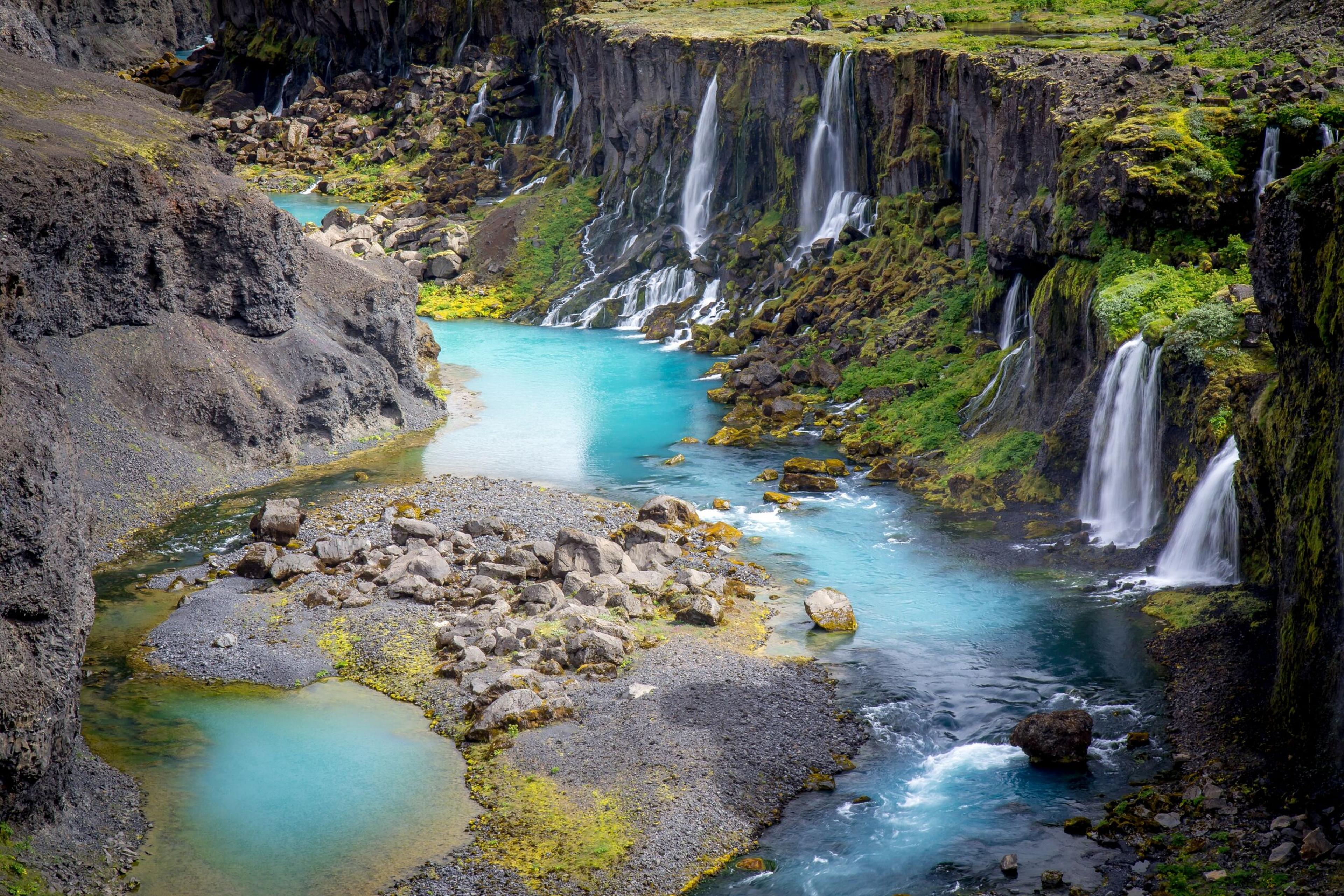 Alt text: "Aerial view of Sigöldugljúfur canyon in Iceland, showing a river meandering through a rugged landscape with multiple small waterfalls cascading into vibrant turquoise pools."