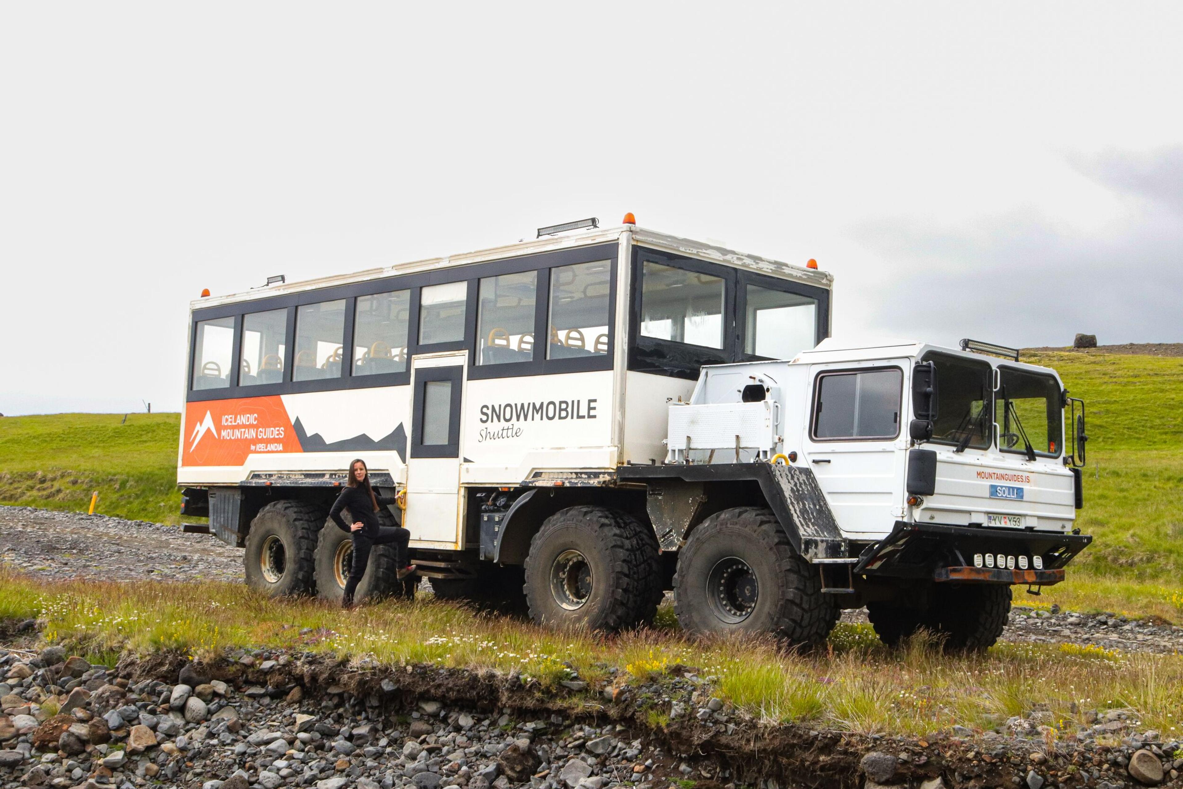 Large off-road mountain truck, parked on rocky terrain with a person standing beside it.