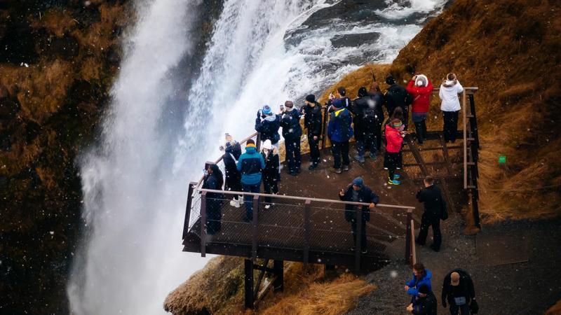 Tourists on an observation deck next to a powerful waterfall, with snow falling.
