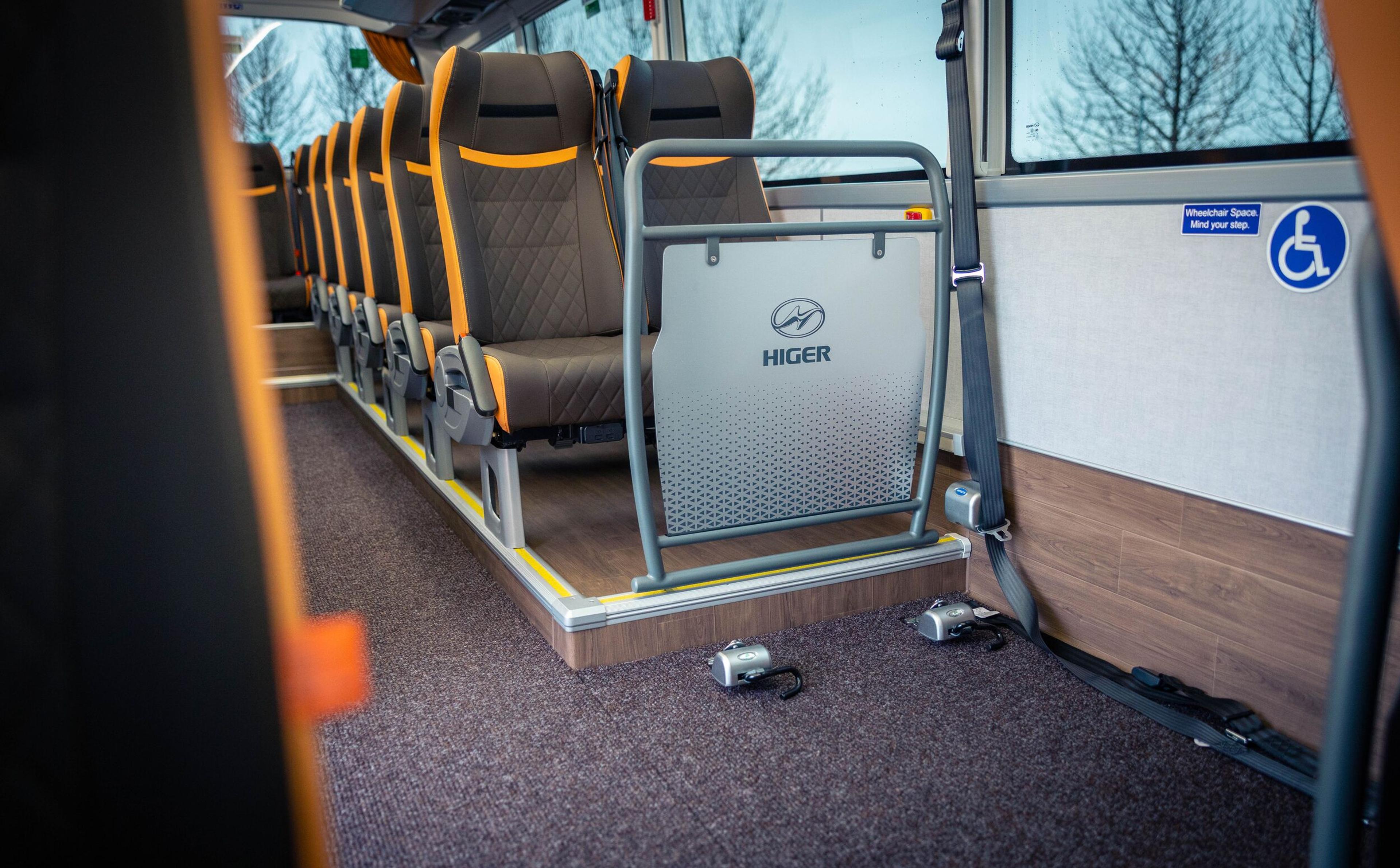 Interior of a Higer bus showing a row of passenger seats and a designated accessible wheelchair area with securing straps.