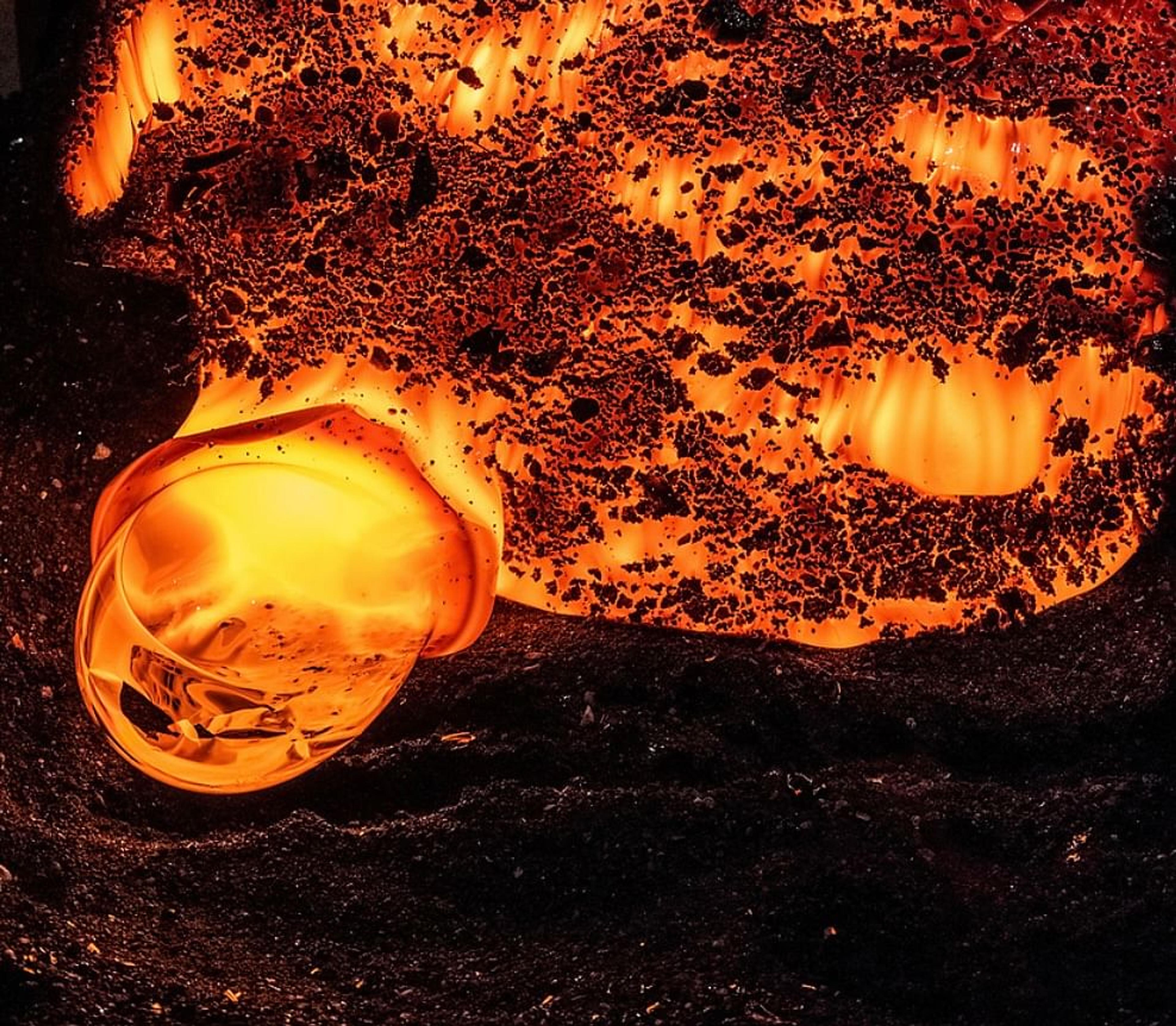 Audience members in a dimly lit room record a glowing, red, molten-like object with their smartphones, several using flash.