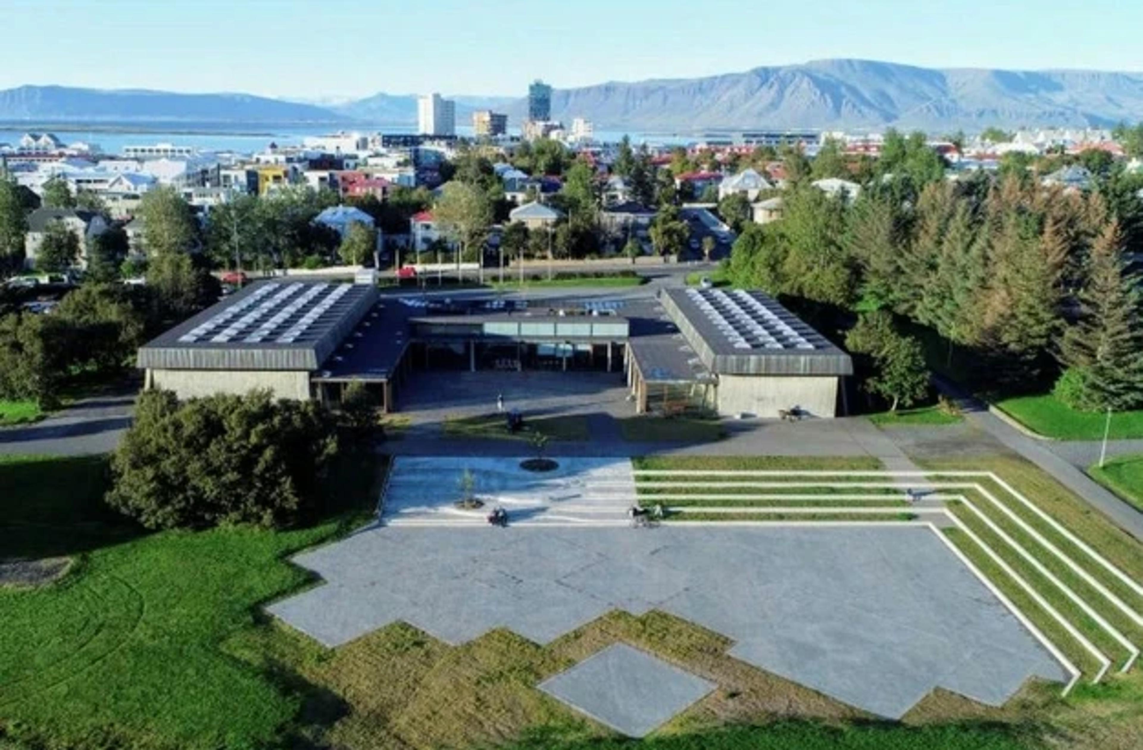 Aerial view of Reykjavík Art Museum Kjarvalsstaðir surrounded by greenery, with the cityscape and mountains in the background.