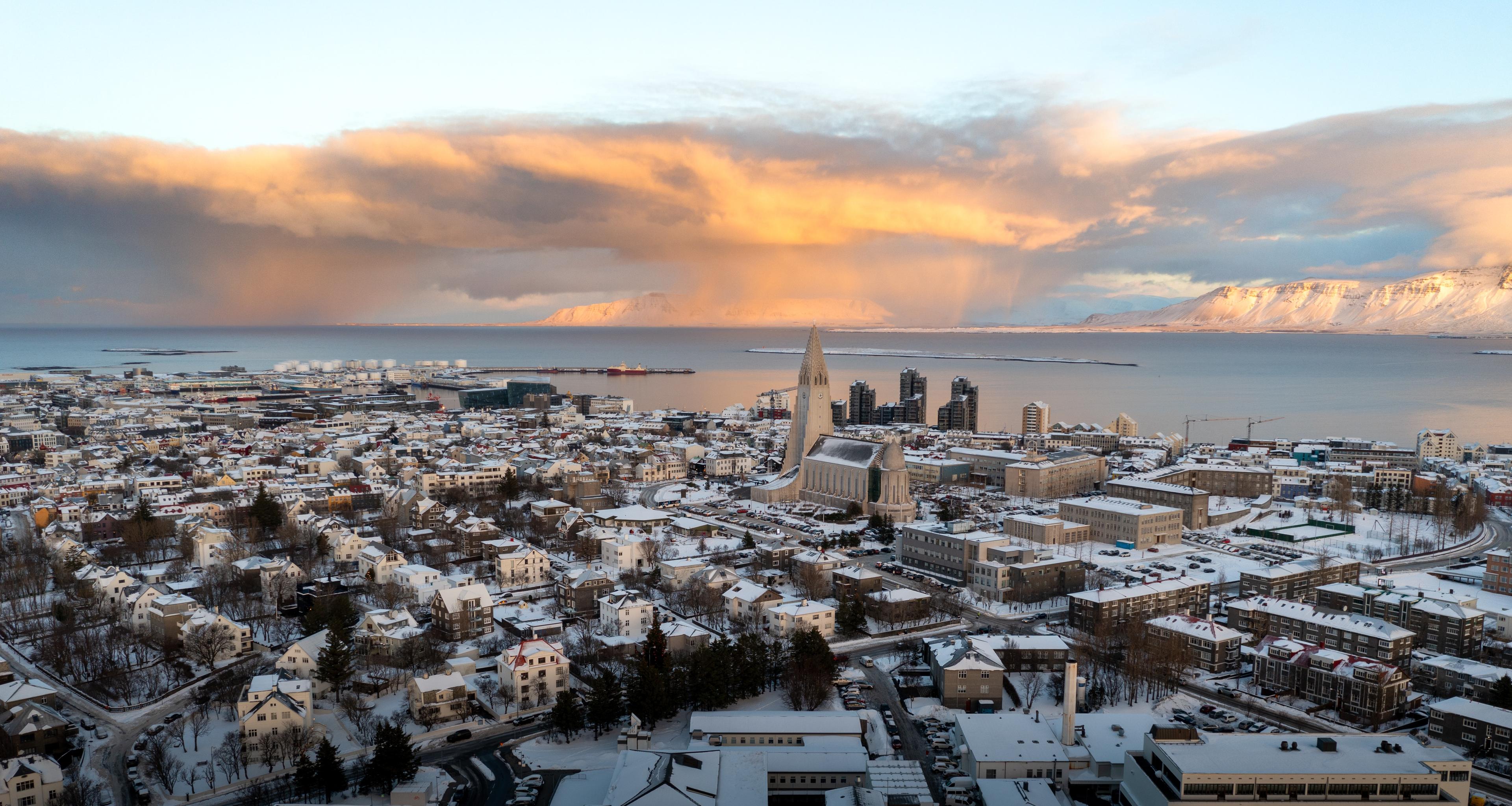 A panoramic view of Reykjavik blanketed in snow at sunrise or sunset, with the iconic Hallgrímskirkja church standing tall amidst the cityscape
