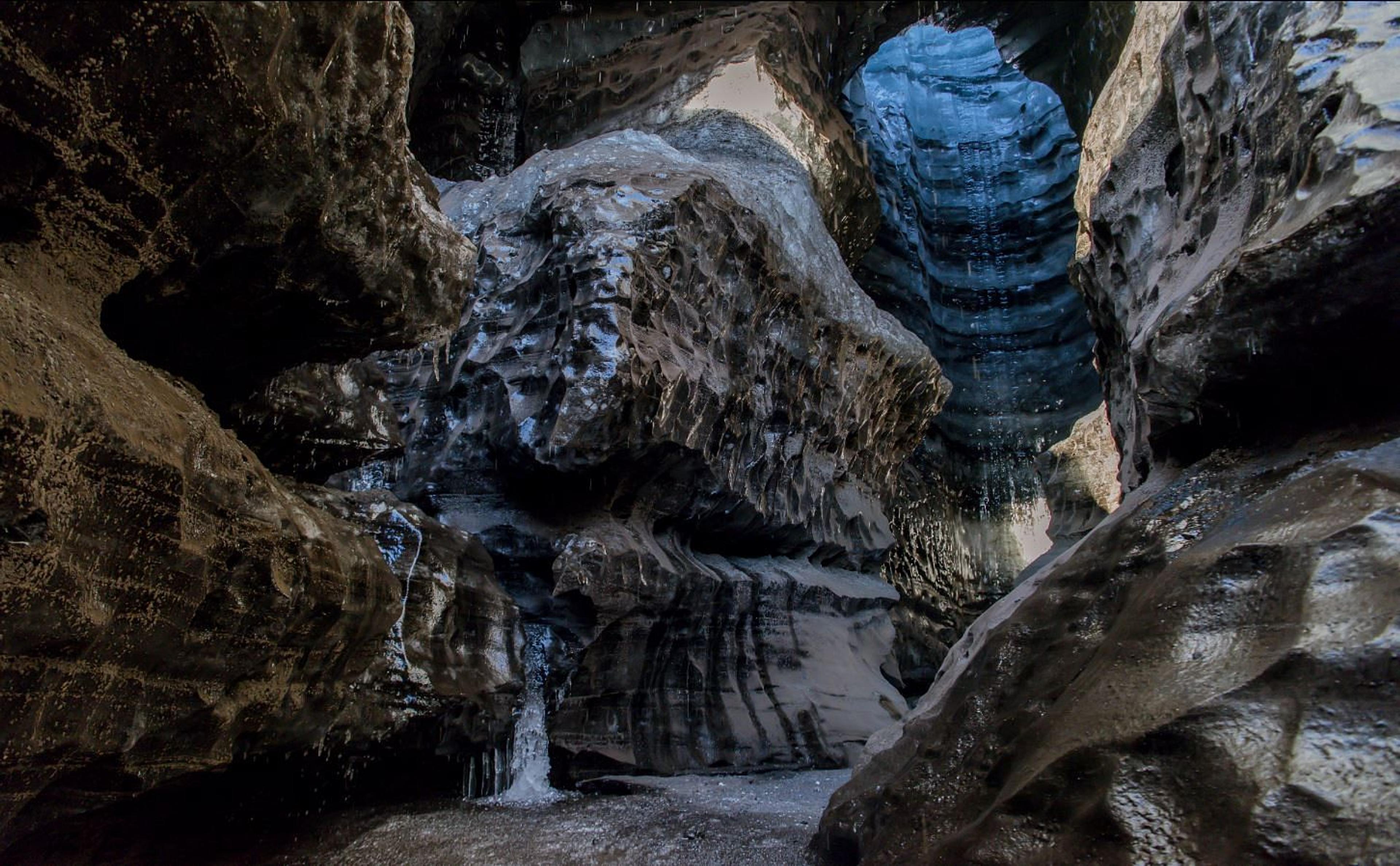 Interior of a dark, textured ice cave with a tall, blue-glowing opening above.