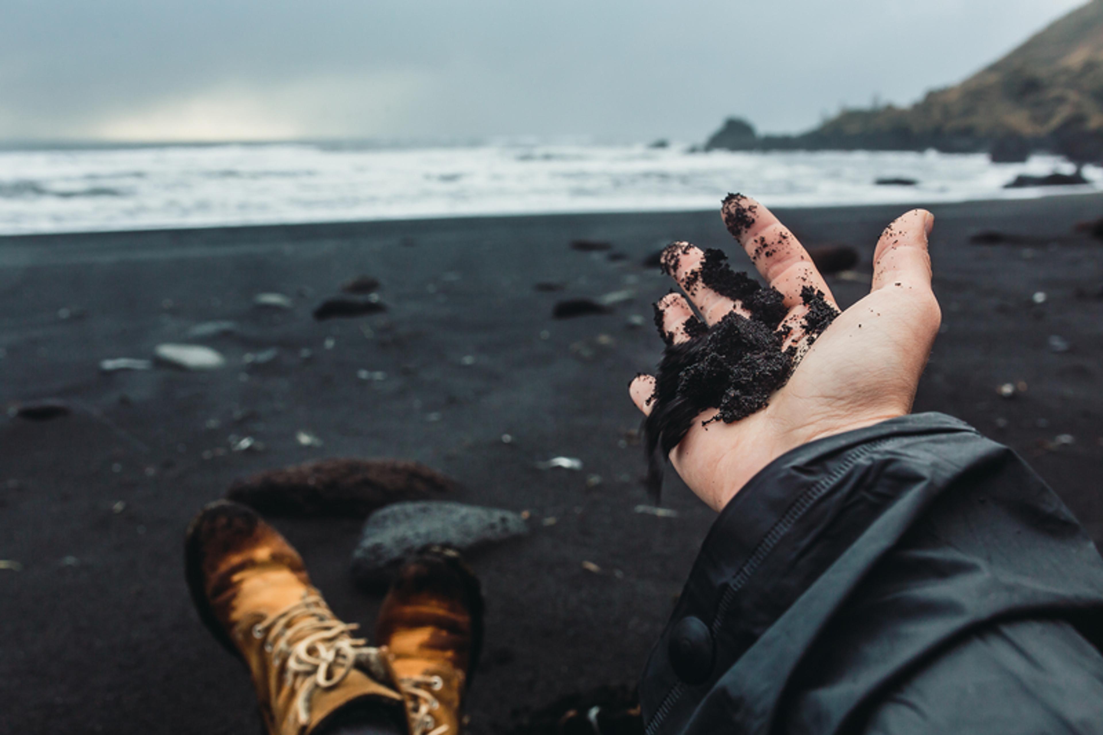 a person is playing with sand on a black sandy beach .