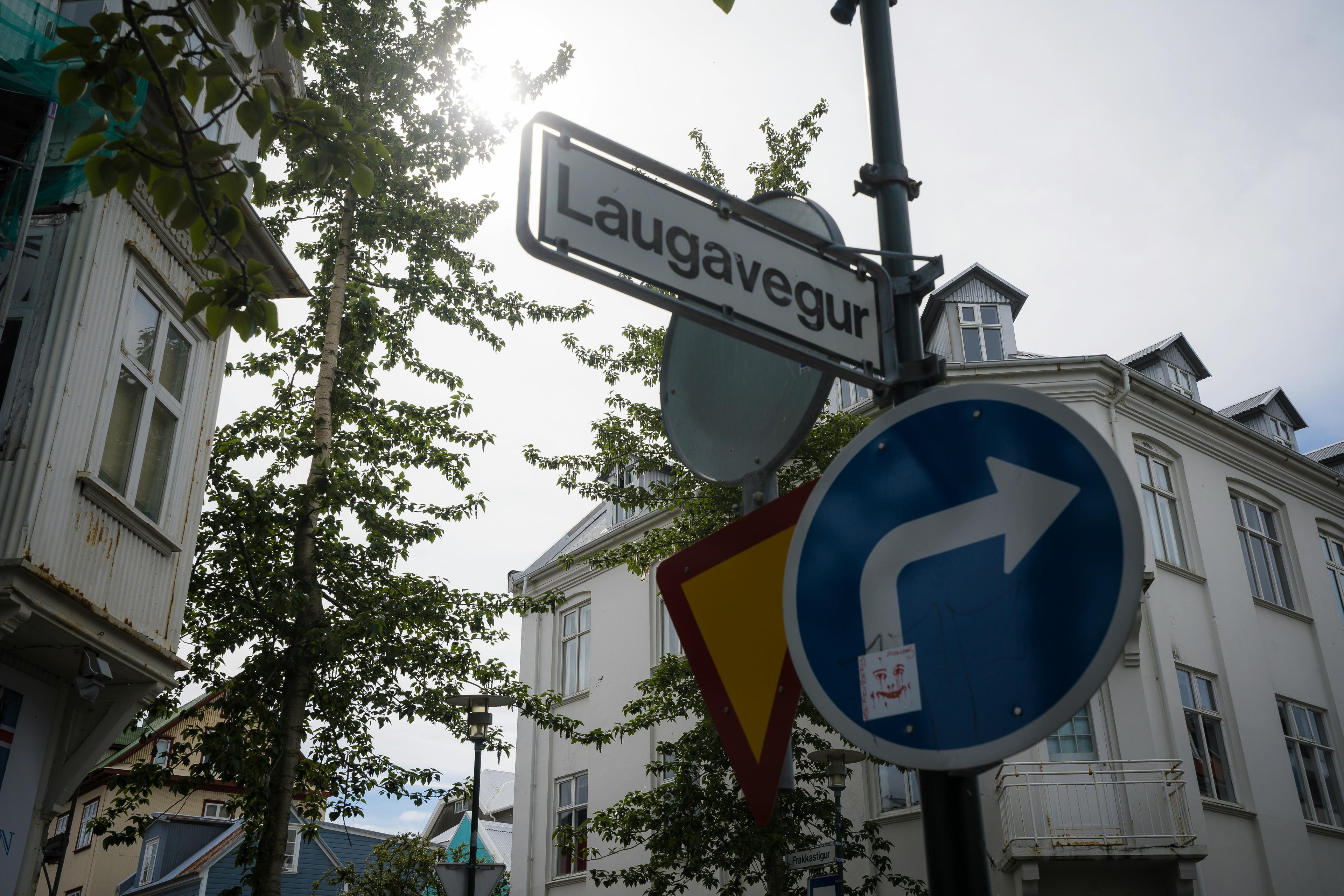 Street sign for Laugavegur with a red building and green window frame in the background.