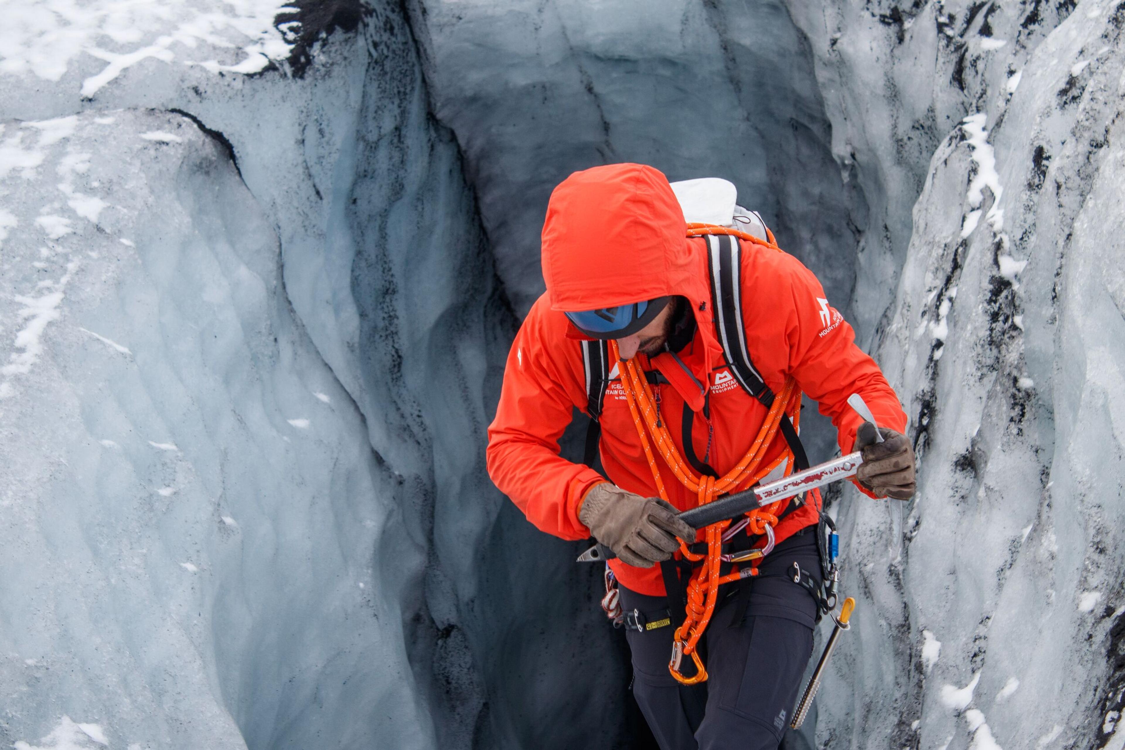 a man in a red jacket is climbing a glacier .