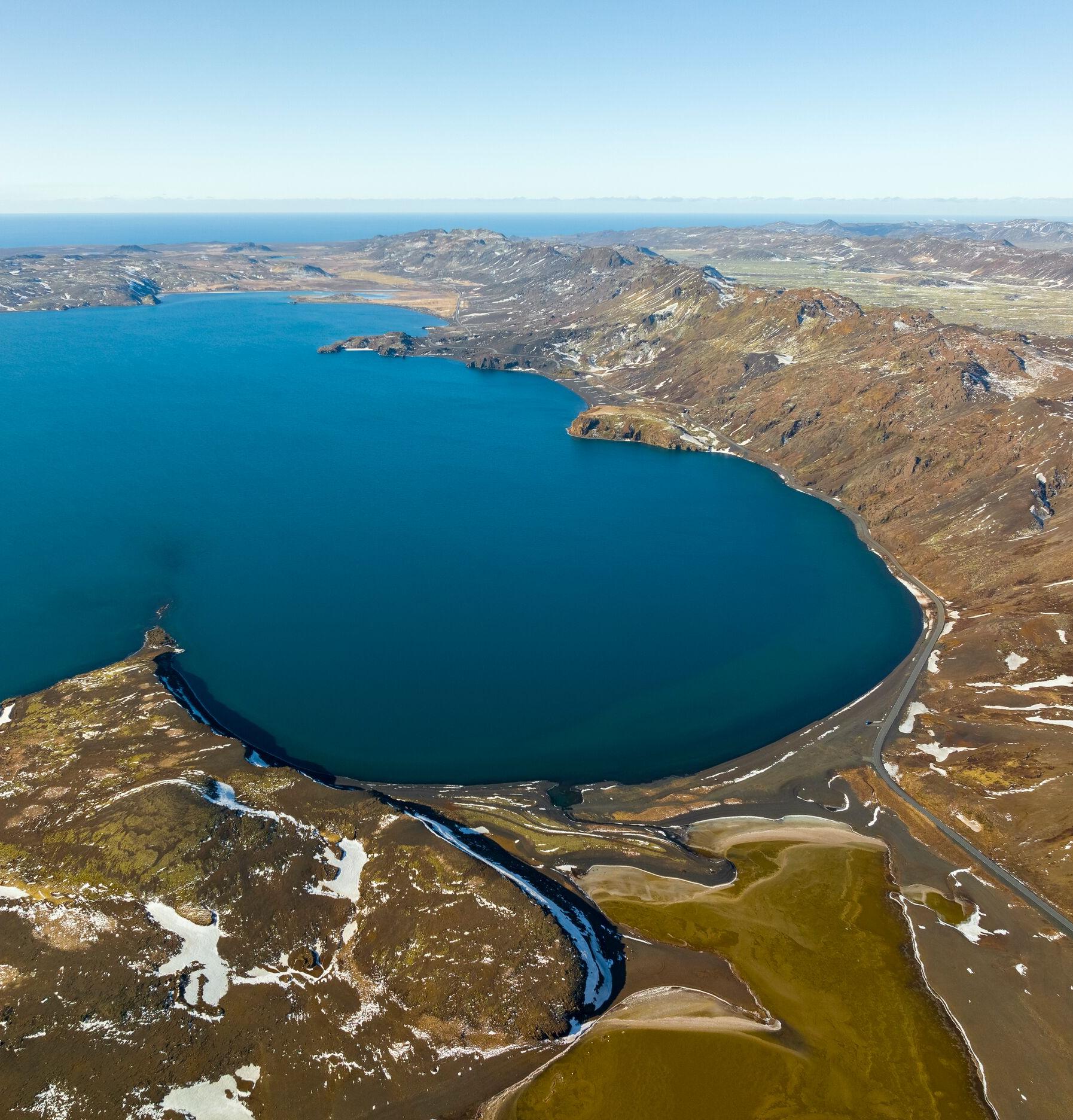 Aerial view of Kleifarvatn Lake, with deep blue waters surrounded by rugged, snow-dusted terrain and winding shorelines.